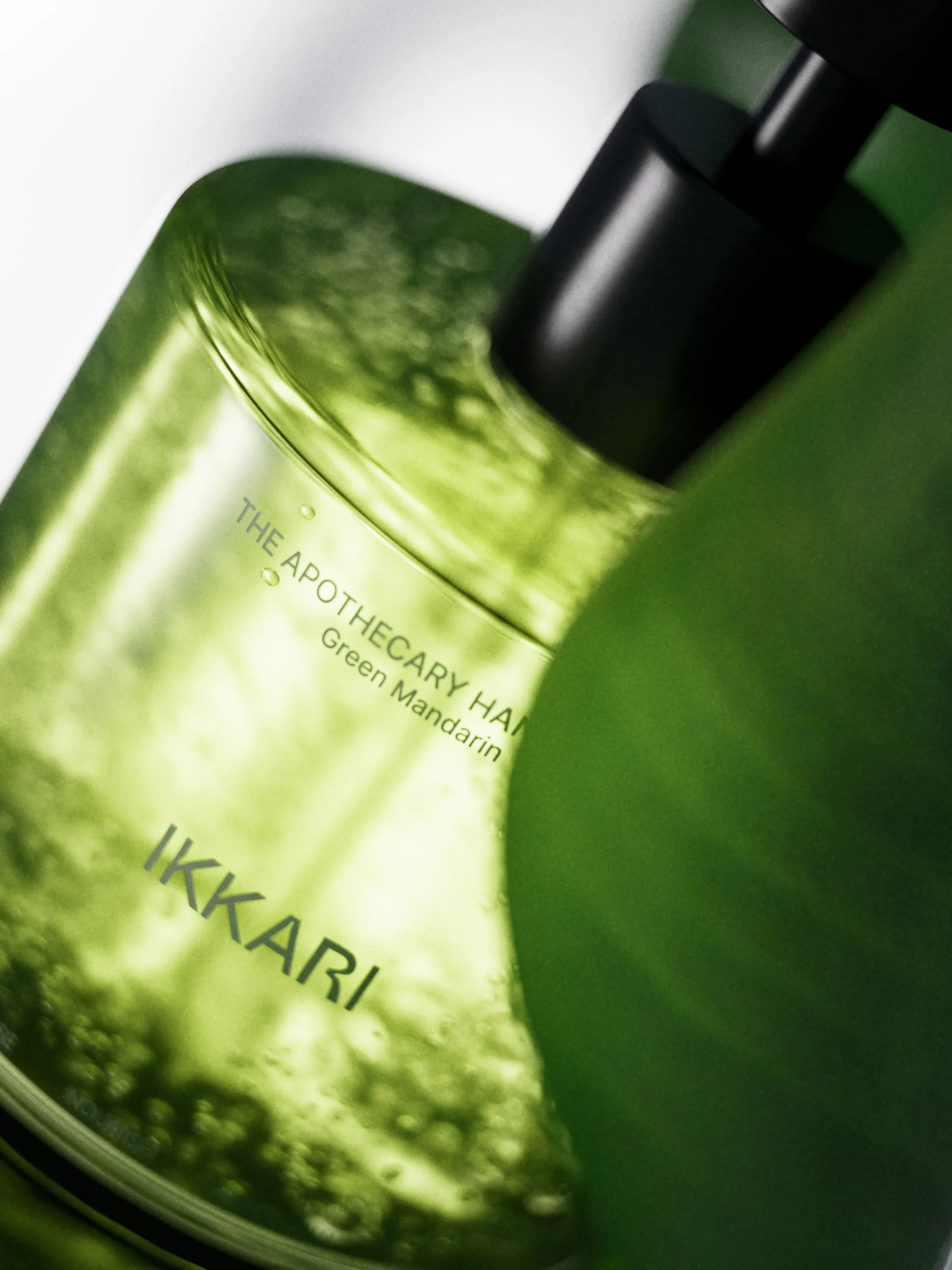 CGI render of a green translucent Green Mandarin hand wash bottle with black pump, shown close up at an angle, for IKKARI.
