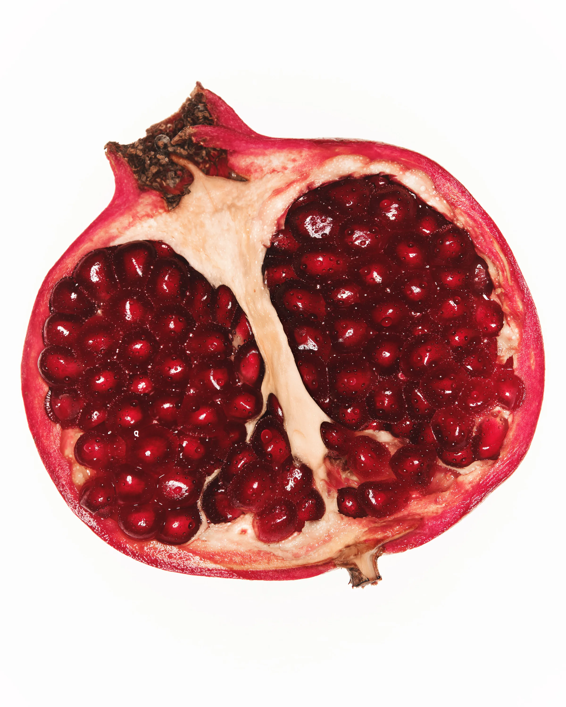 Still life of a halved pomegranate with glossy red seeds on a white background, for Kylie Cosmetics.