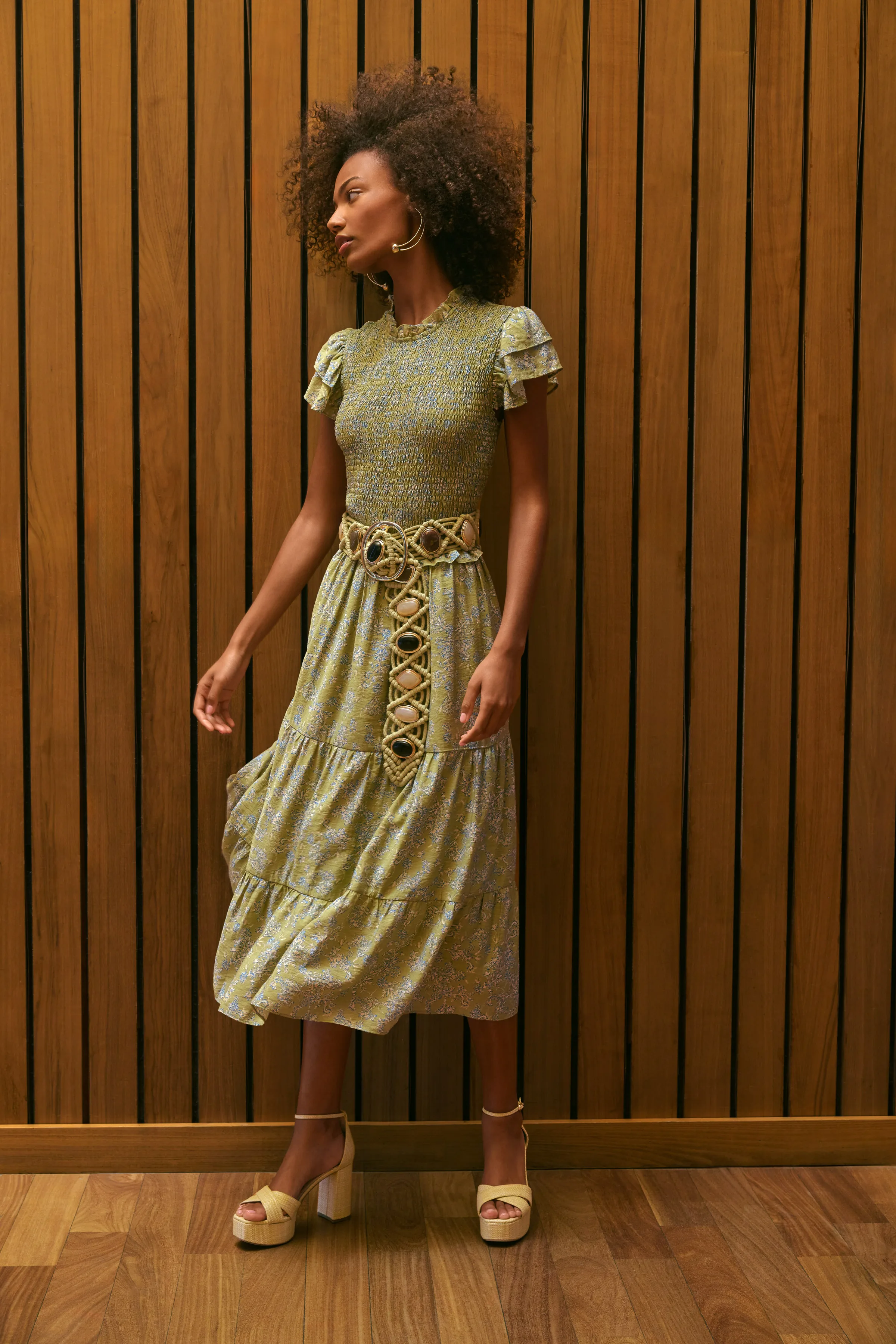 Model in a smocked green floral tiered midi dress, rope belt and platform sandals against a wood slat wall, for Sam Edelman.