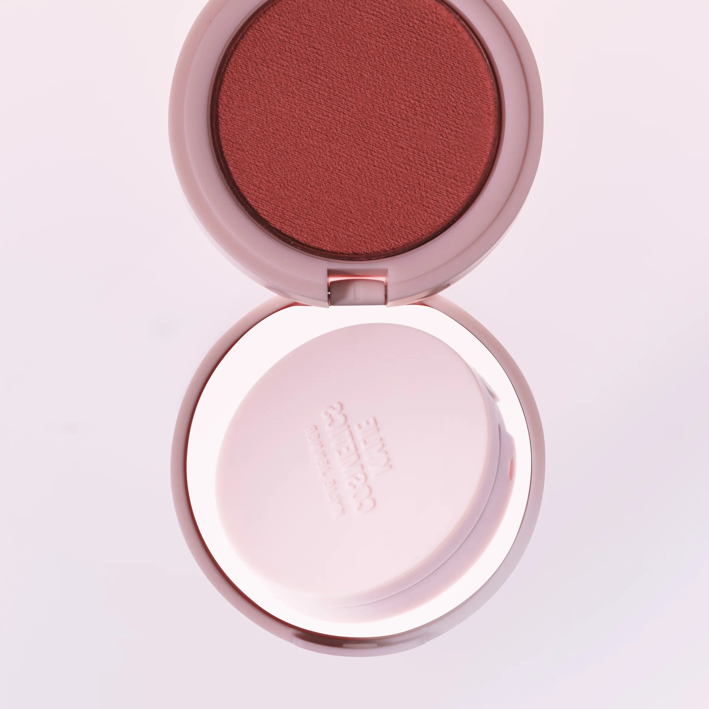 Open pink blush compact with a terracotta powder pan, shot from above on a pale pink background, for Kylie Cosmetics.