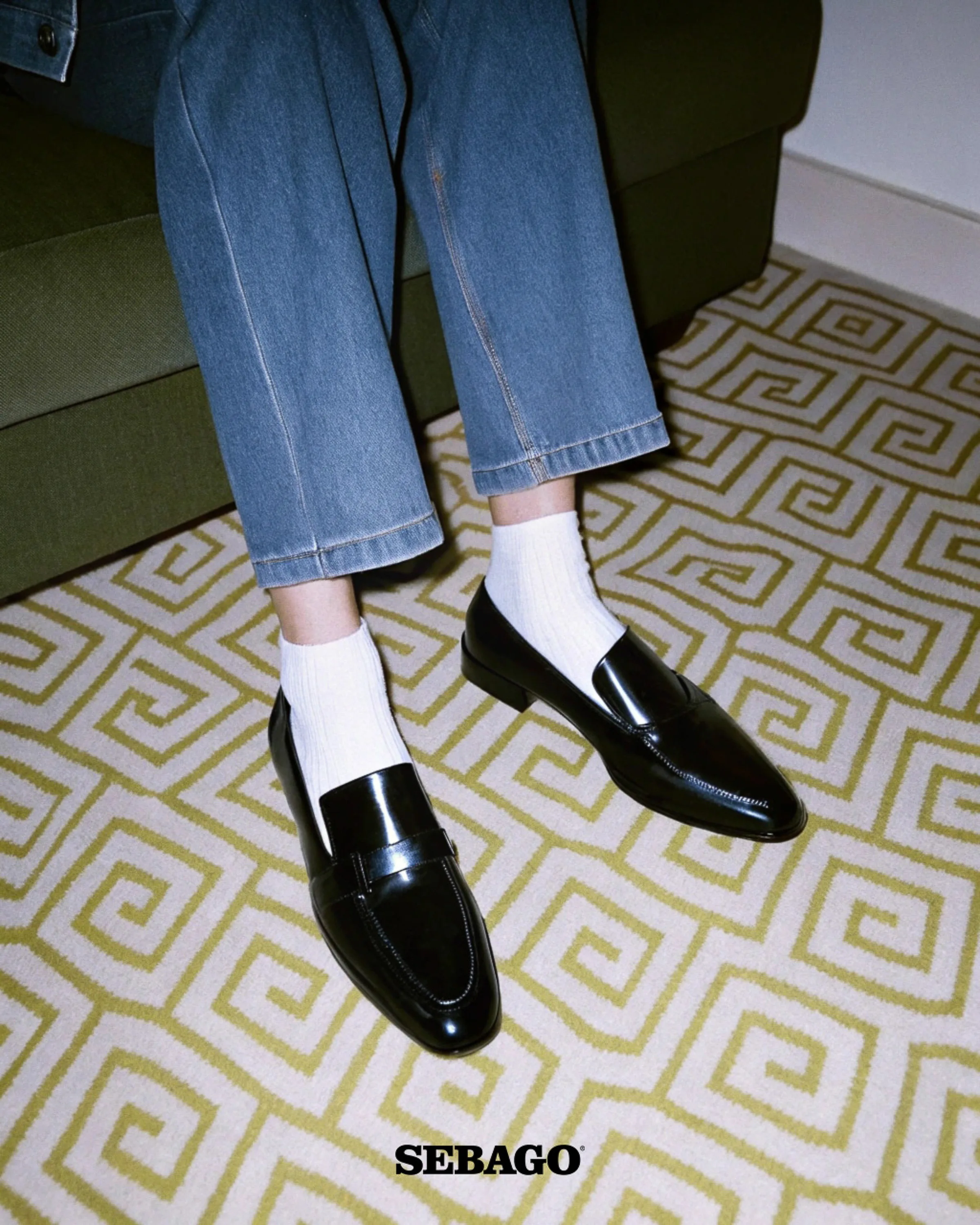AI image of black leather penny loafers with white ribbed socks and cuffed jeans on a green geometric rug. Sebago AI Concept.