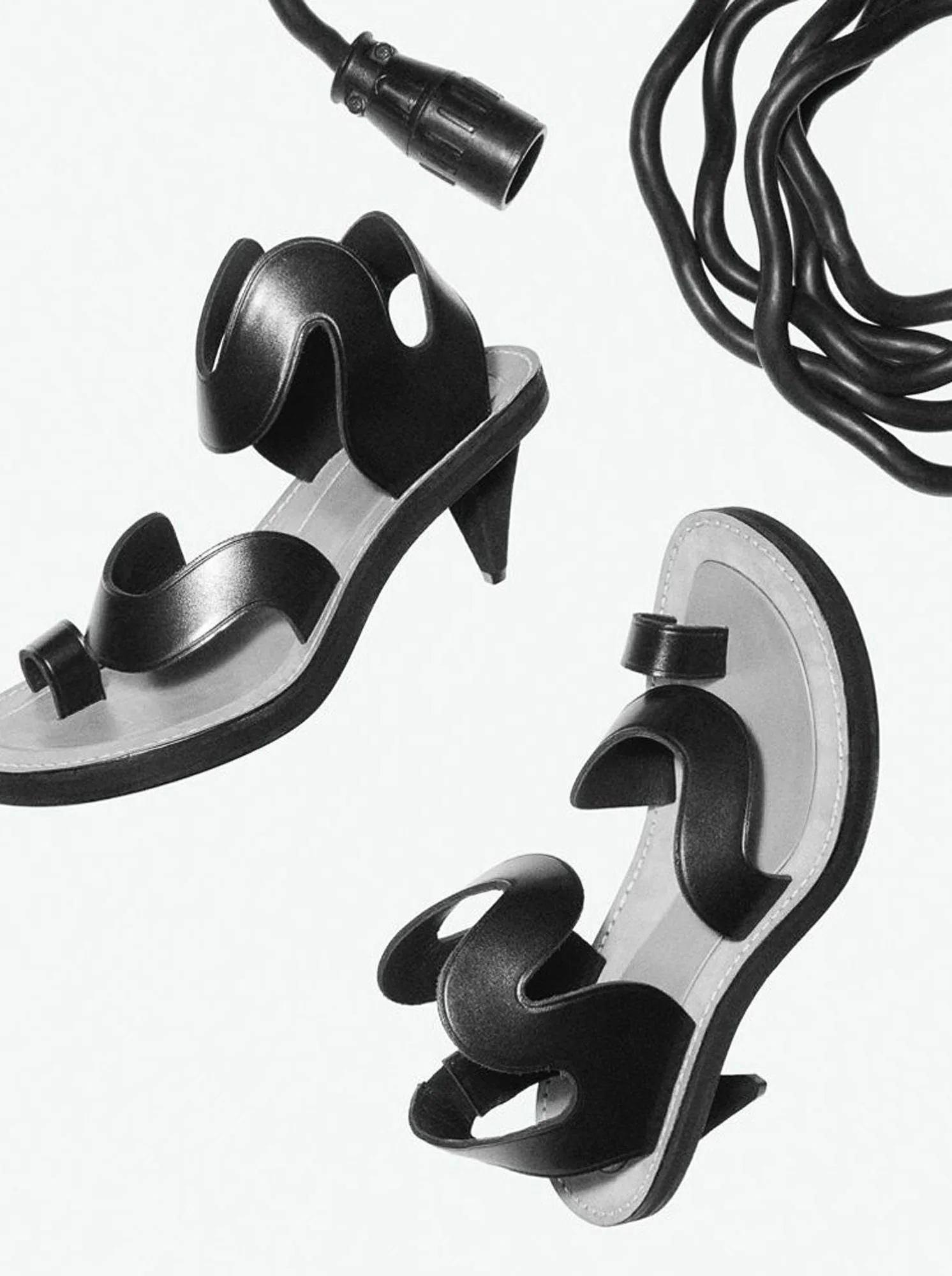 Black sculptural leather toe-ring sandals with cone heels beside coiled black cables on a white background, for Interview Magazine.