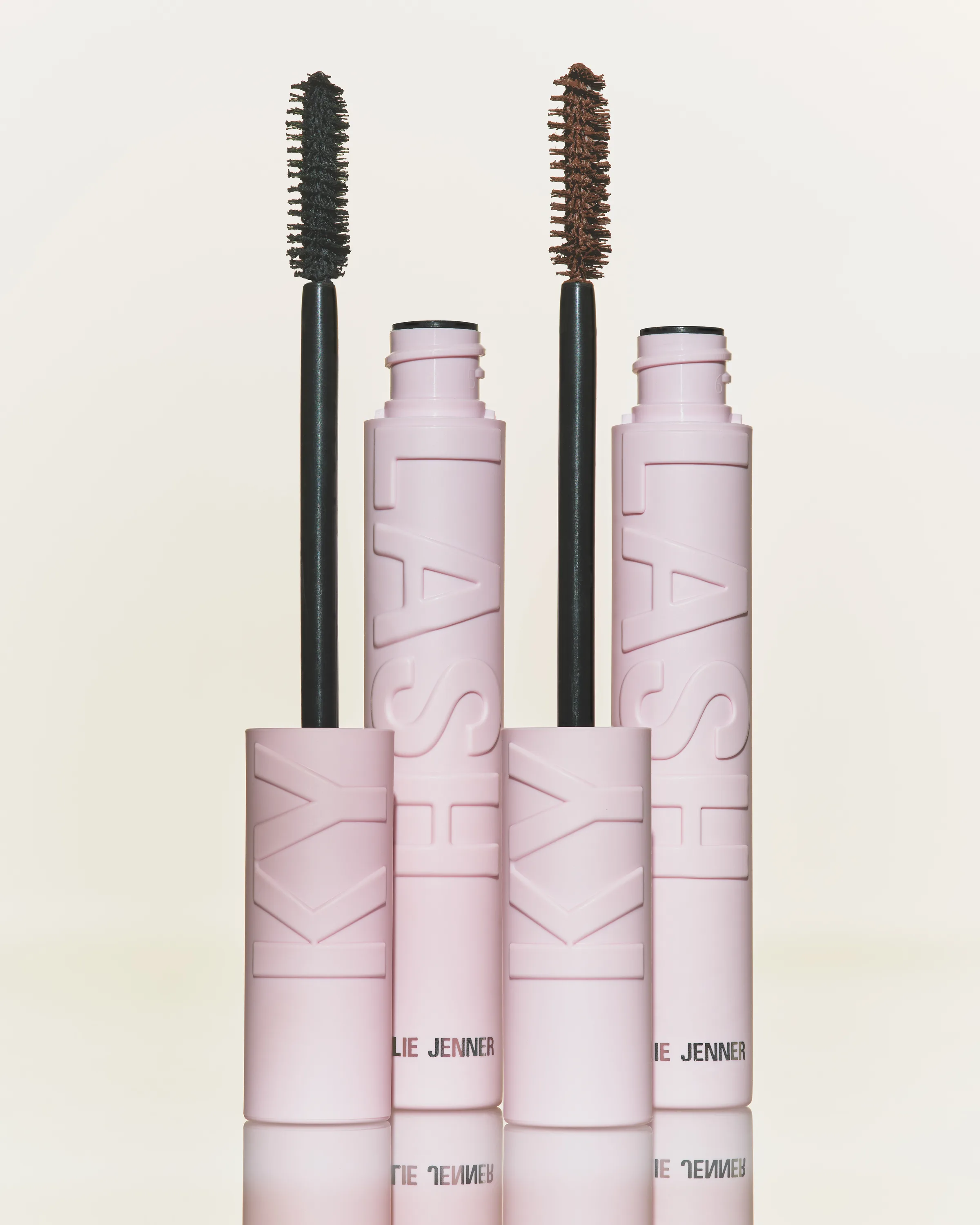 Two pink Kylash mascara tubes with black and brown wands standing on a reflective surface, for Kylie Cosmetics.