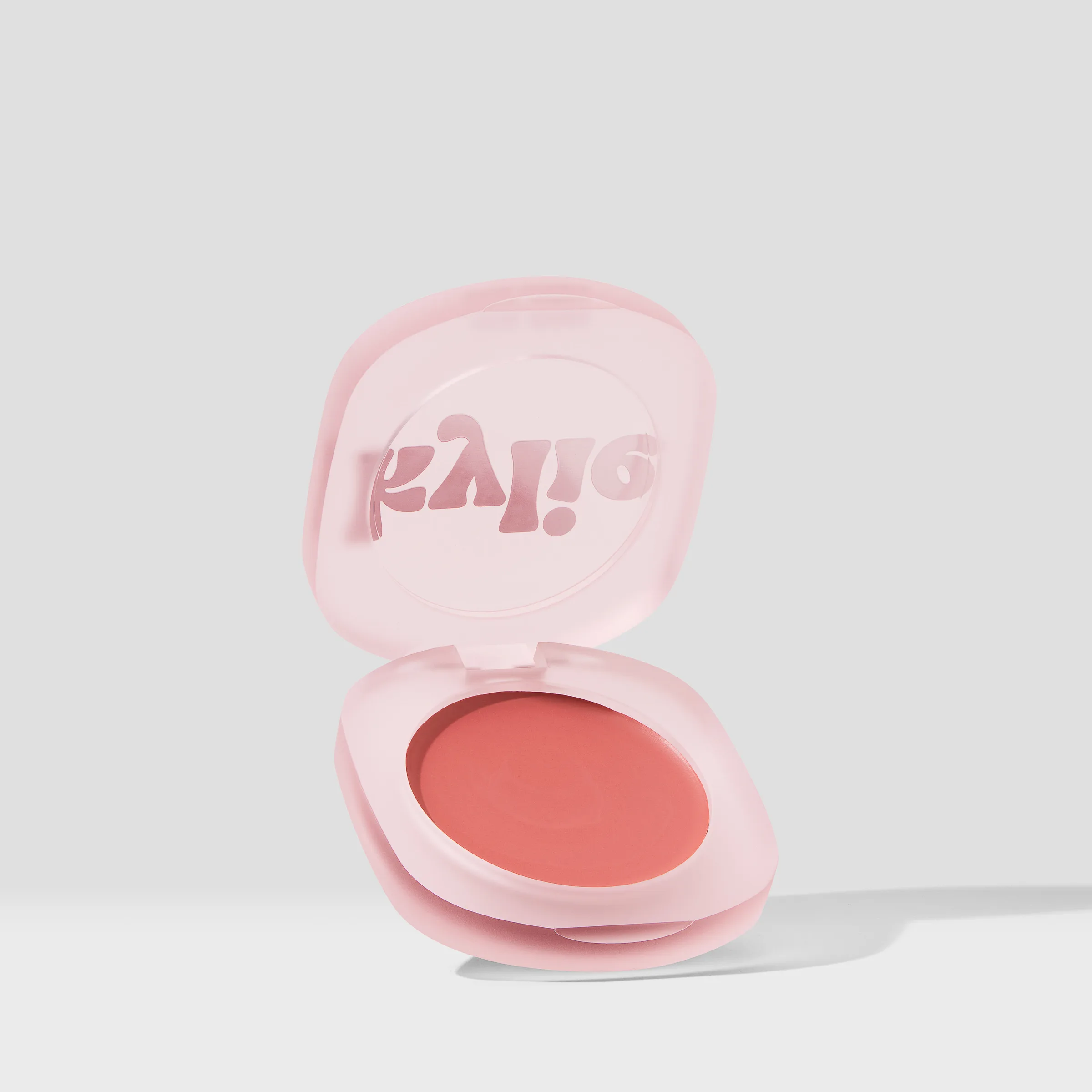 Open pink frosted compact of coral cream blush, propped upright on a light grey background, for Kylie Cosmetics.