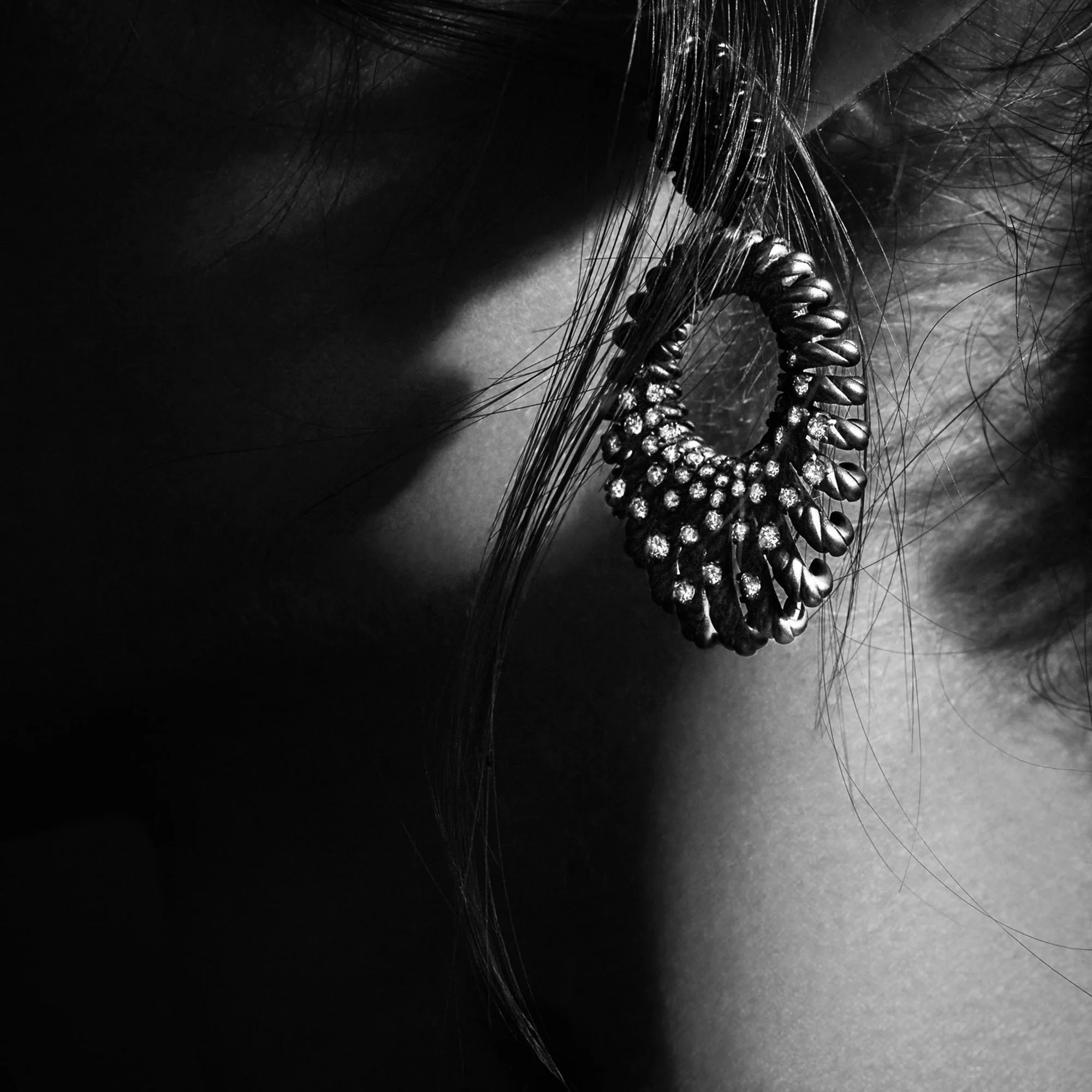 Black-and-white close-up of a diamond-studded cable hoop earring on a model's ear, framed by loose hair, for David Yurman.