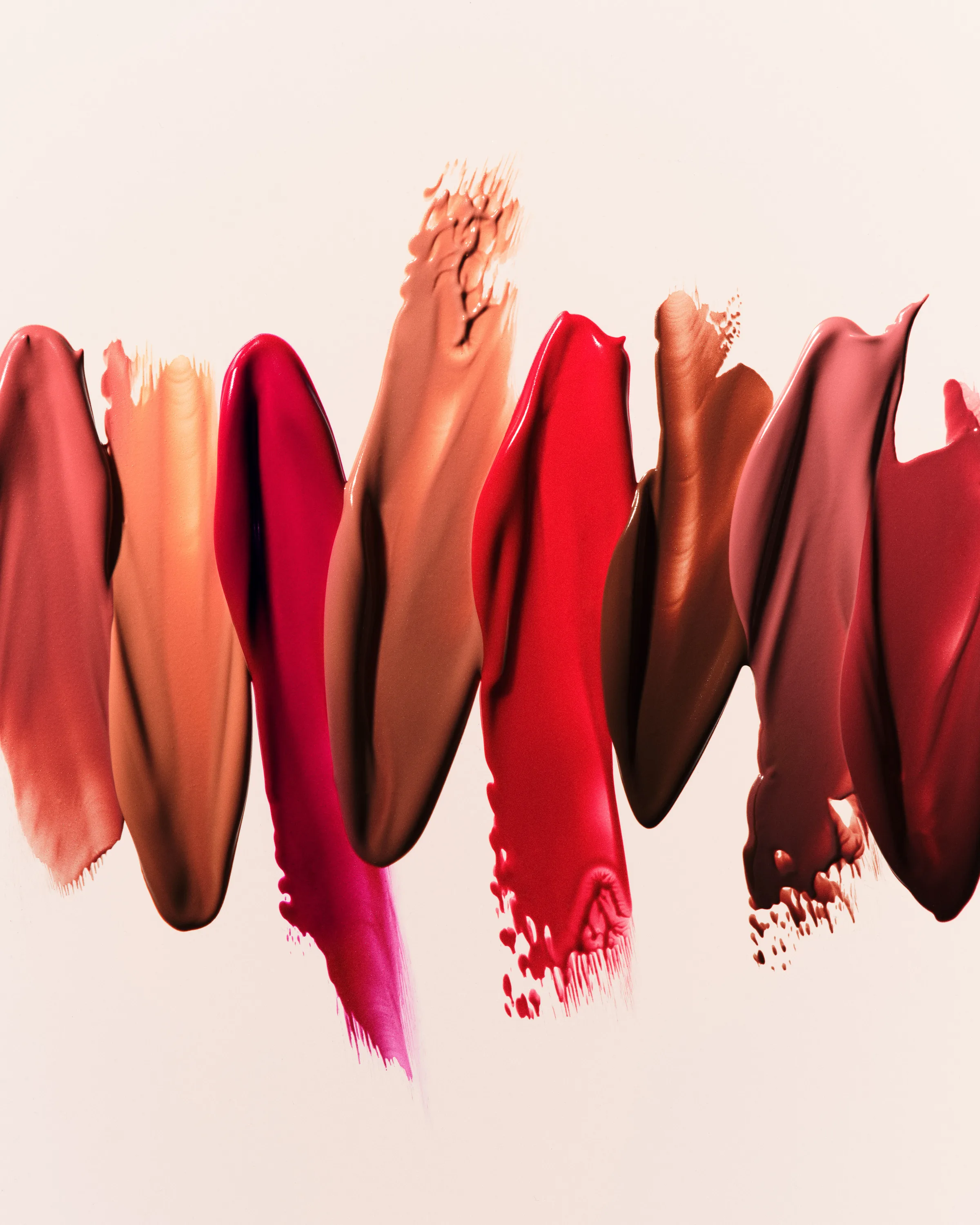 Row of creamy lipstick swatches in nude, pink, red and brown shades smeared across a pale backdrop, for Kylie Cosmetics.