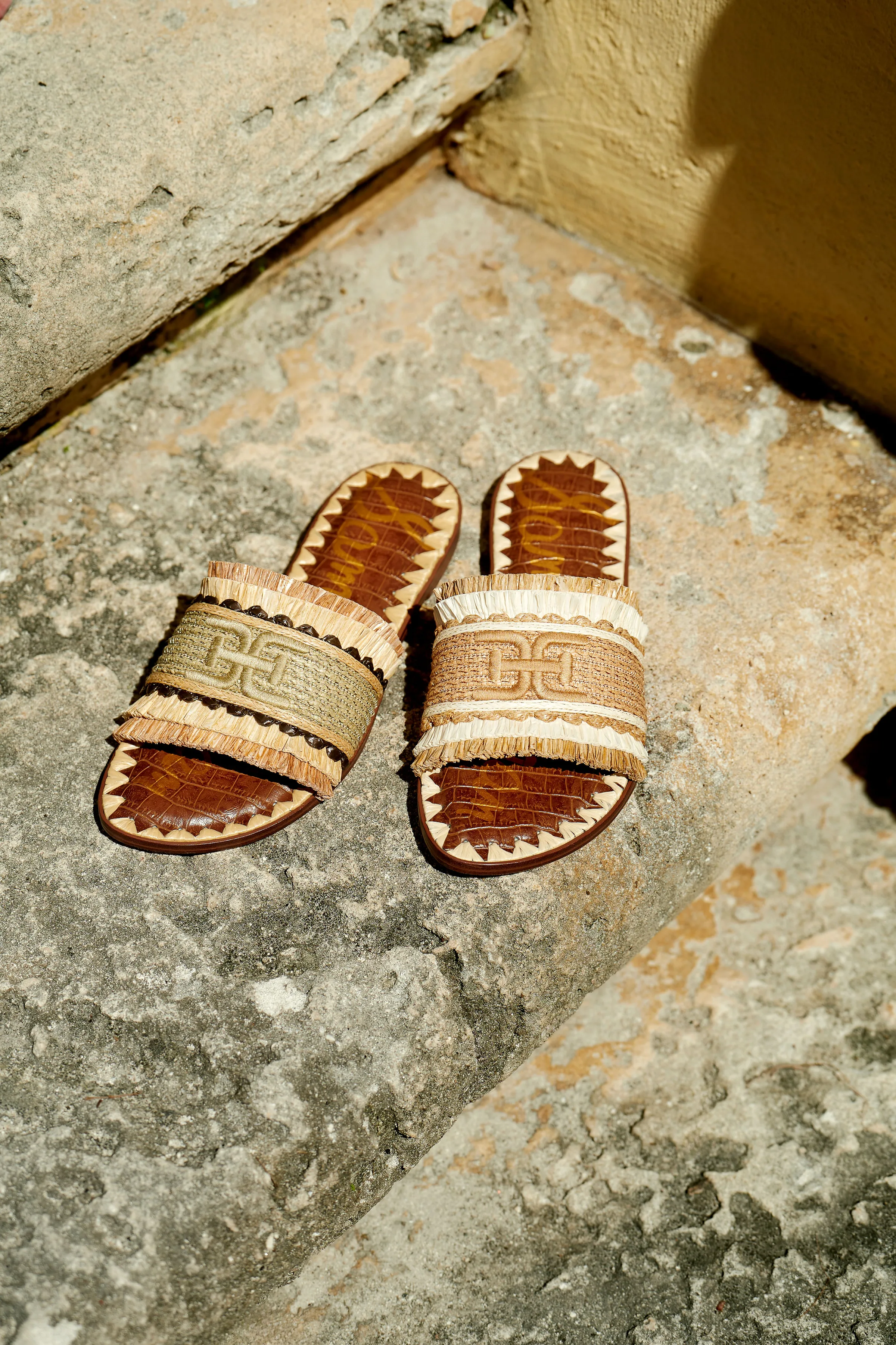 Woven raffia slide sandals with croc-embossed footbeds and double-E logo on sunlit stone steps, for Sam Edelman.