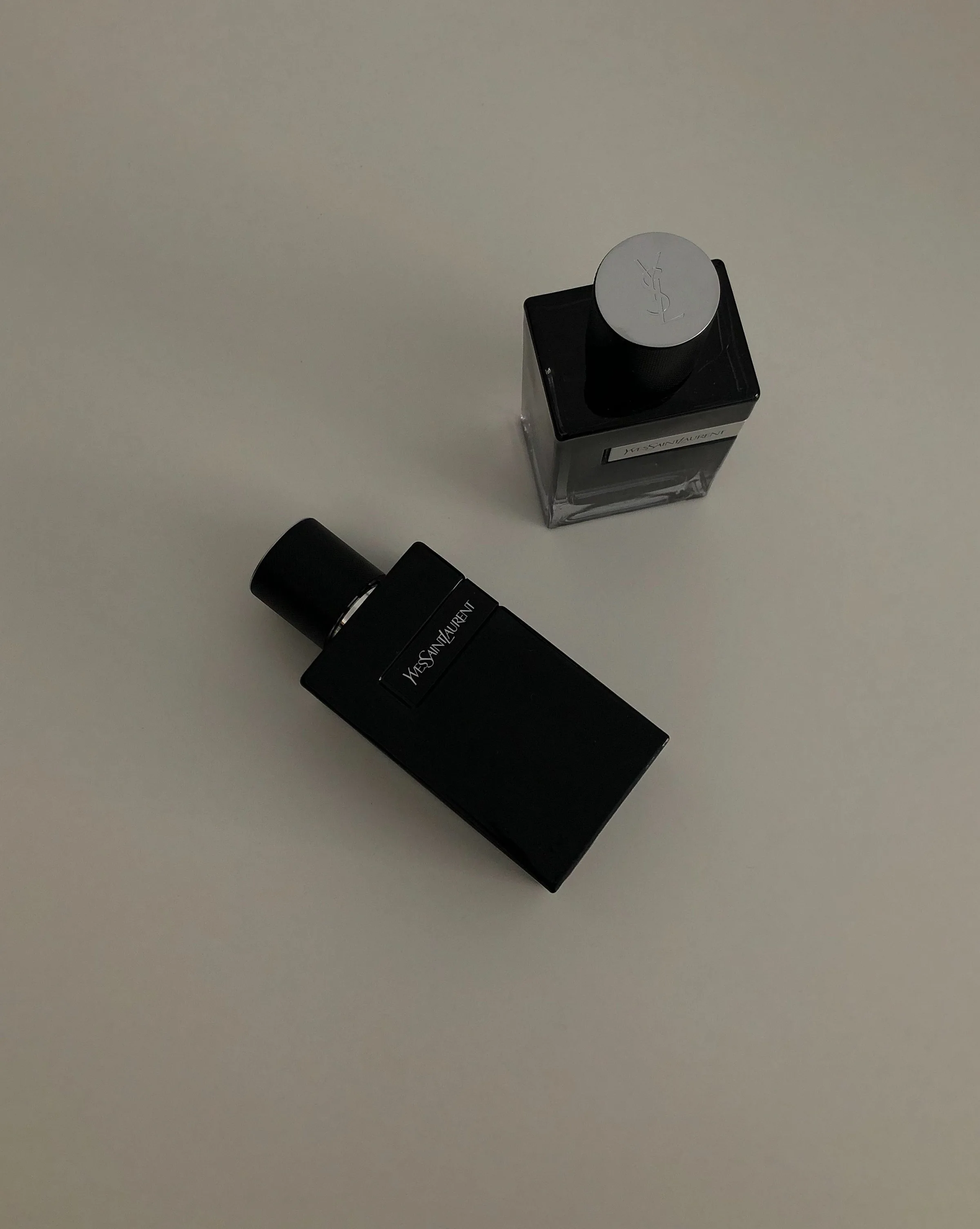 Two black Yves Saint Laurent fragrance bottles shot from above on a pale grey surface, for Yves Saint Laurent.