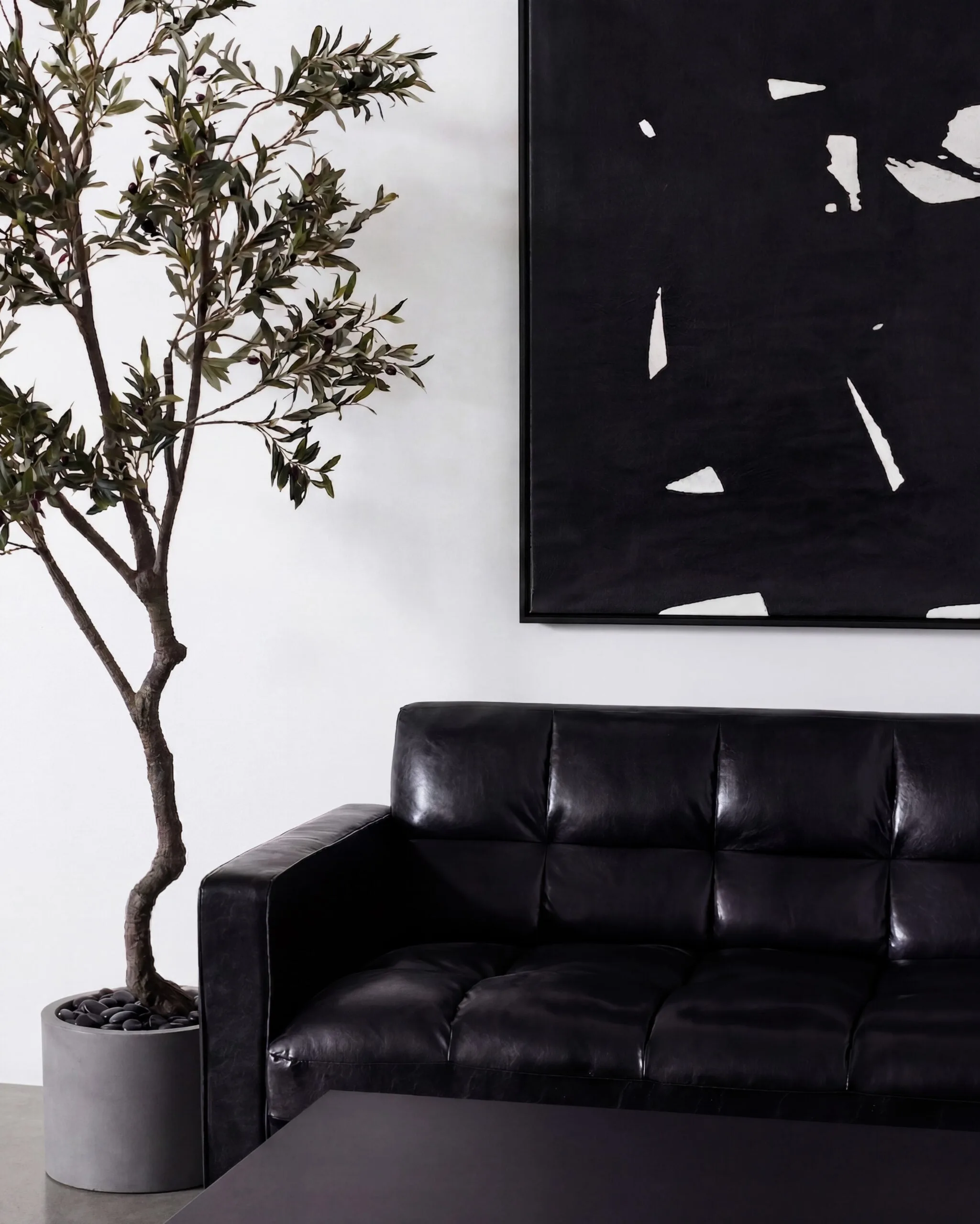 Lounge in Studio 1, Long Island City, with a black leather sofa, potted olive tree and black abstract painting.