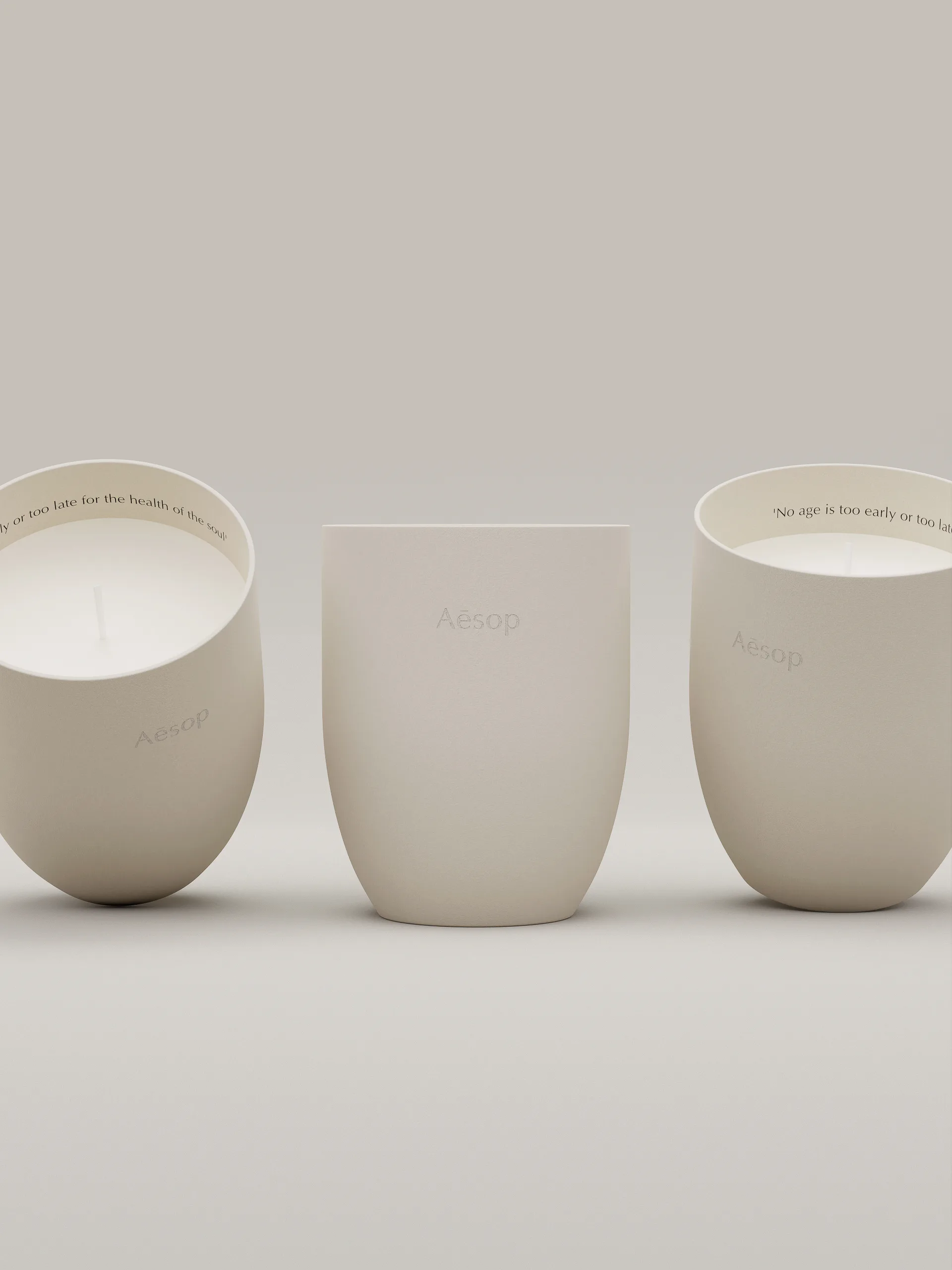 CGI render of three cream ceramic candle vessels, two tilted showing white wax, on a pale grey backdrop, for Aesop.