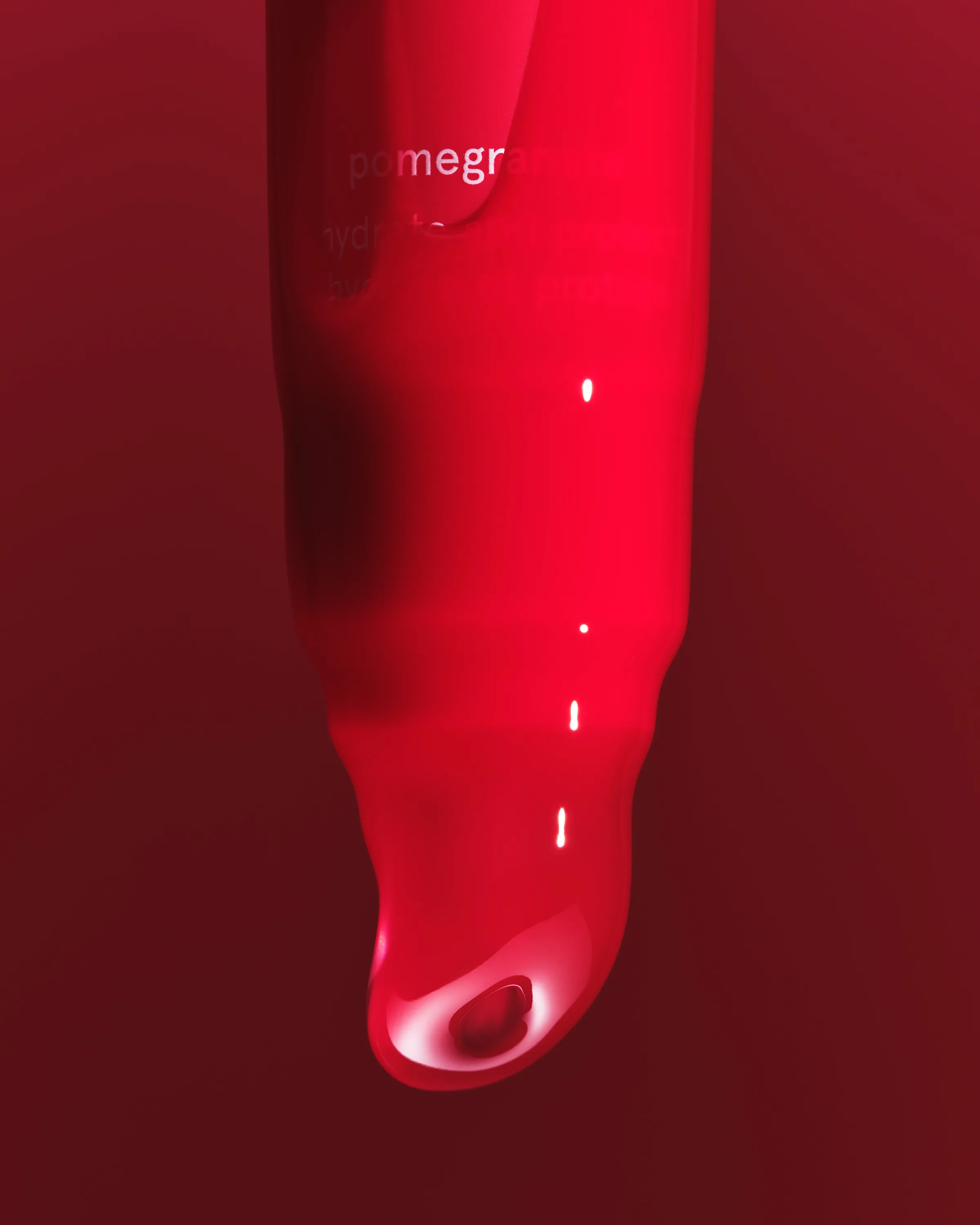 Close-up of a glossy red pomegranate lip product tube tip with a droplet on a deep red background, for Kylie Cosmetics.