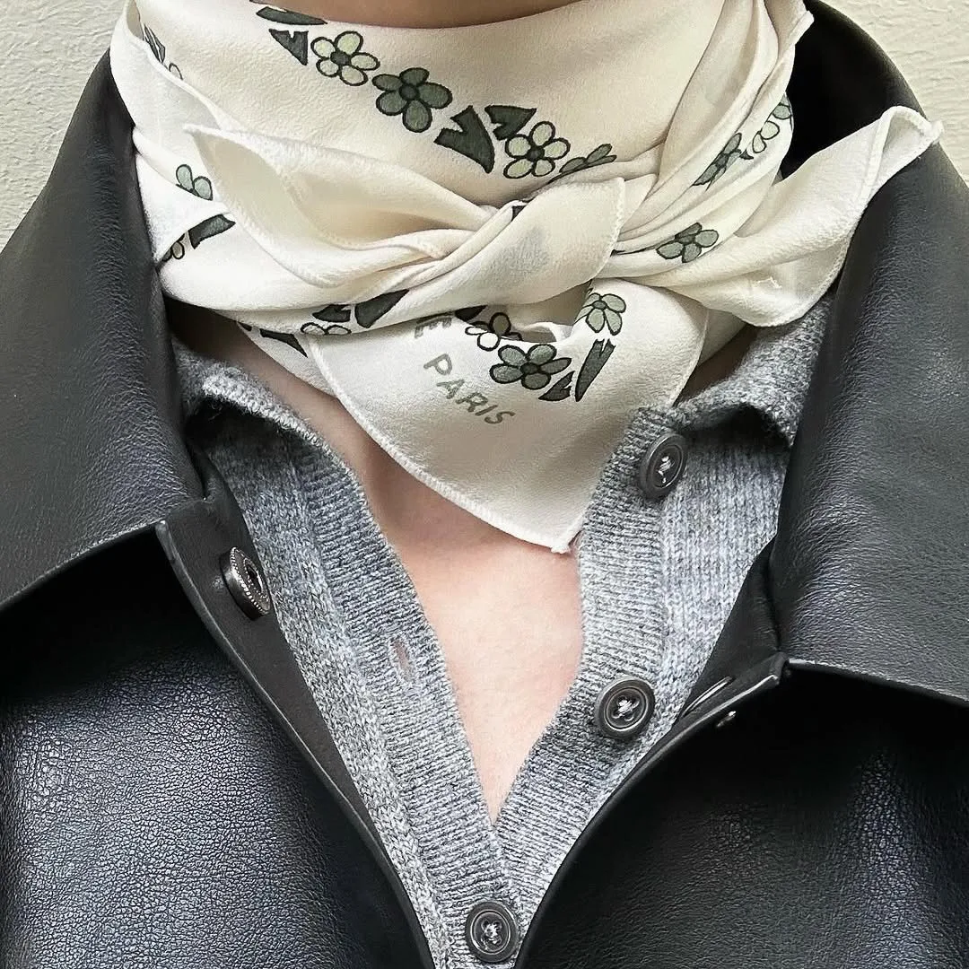 Cream silk scarf with green floral print knotted at the neck over a grey cardigan and black leather jacket.