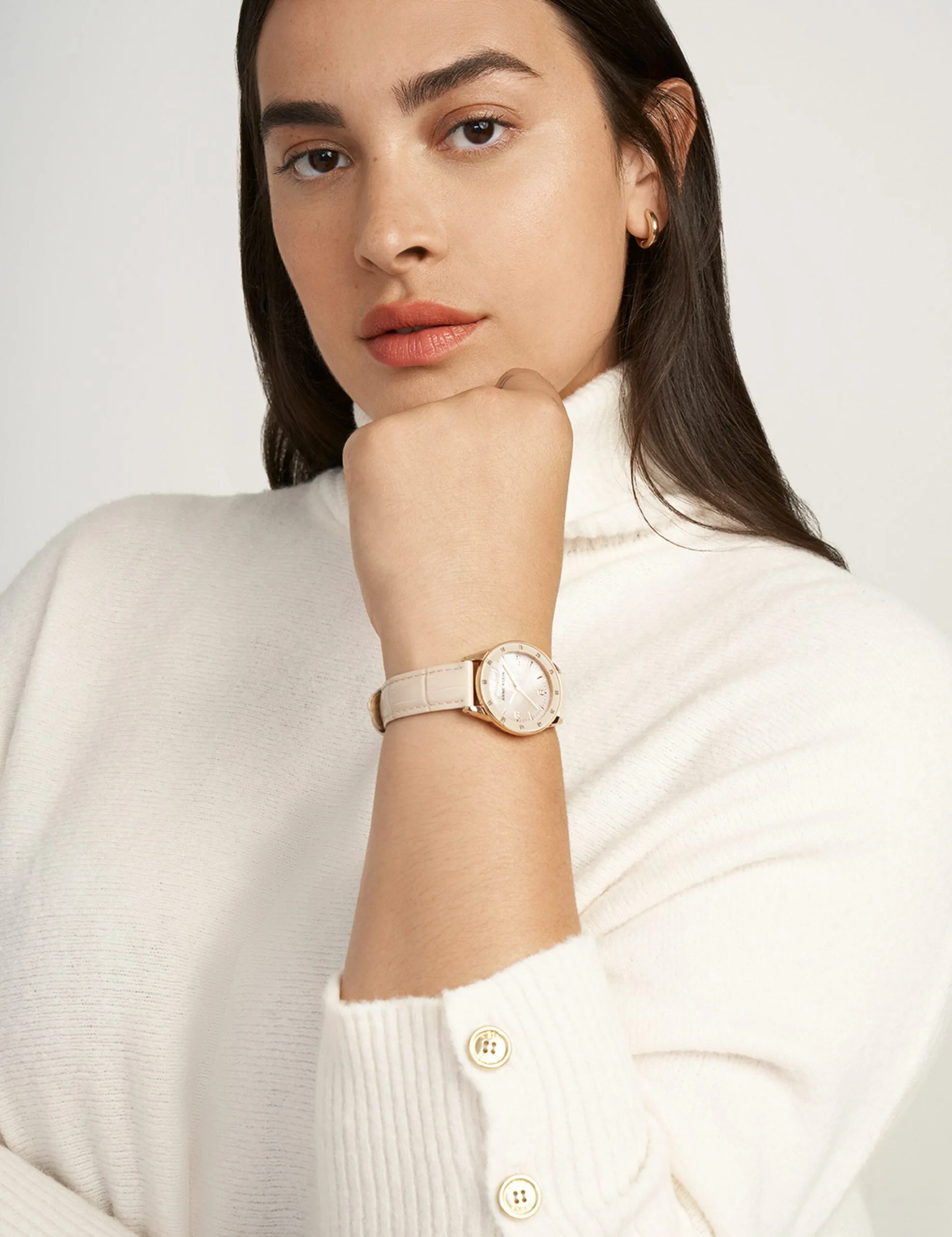 Model in a cream turtleneck sweater wearing a rose gold watch with a blush leather strap, for Anne Klein.