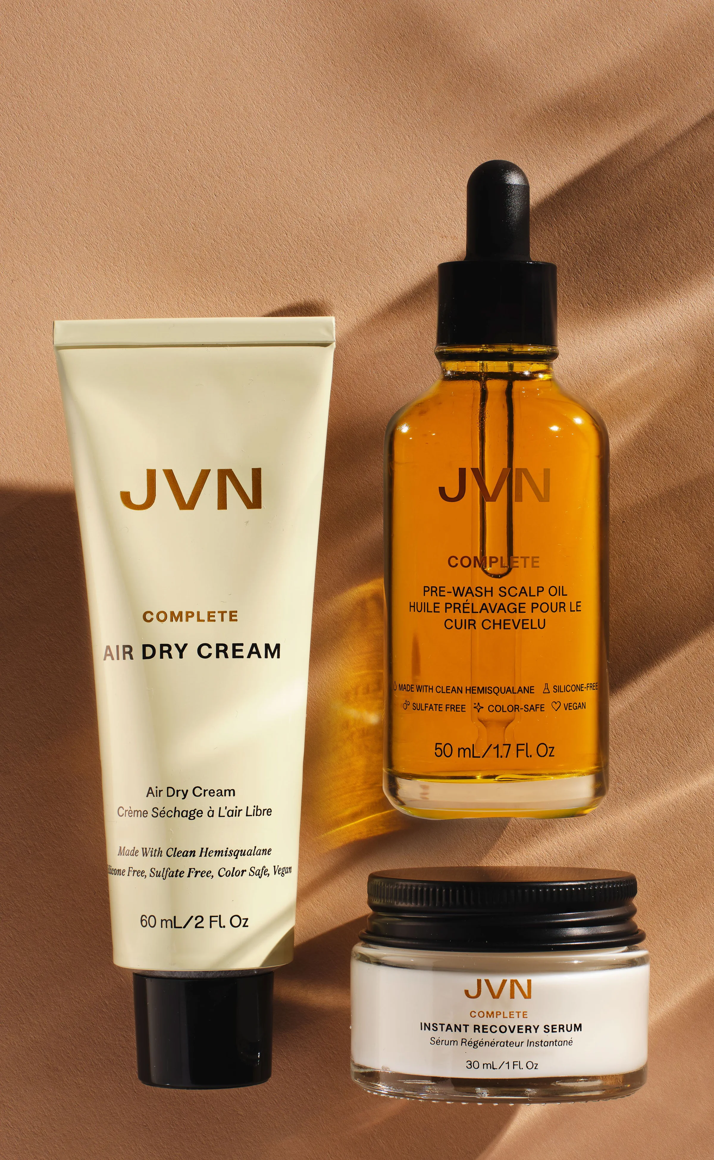 Air Dry Cream tube, pre-wash scalp oil bottle and recovery serum jar on tan backdrop with sunlit shadows, for JVN.