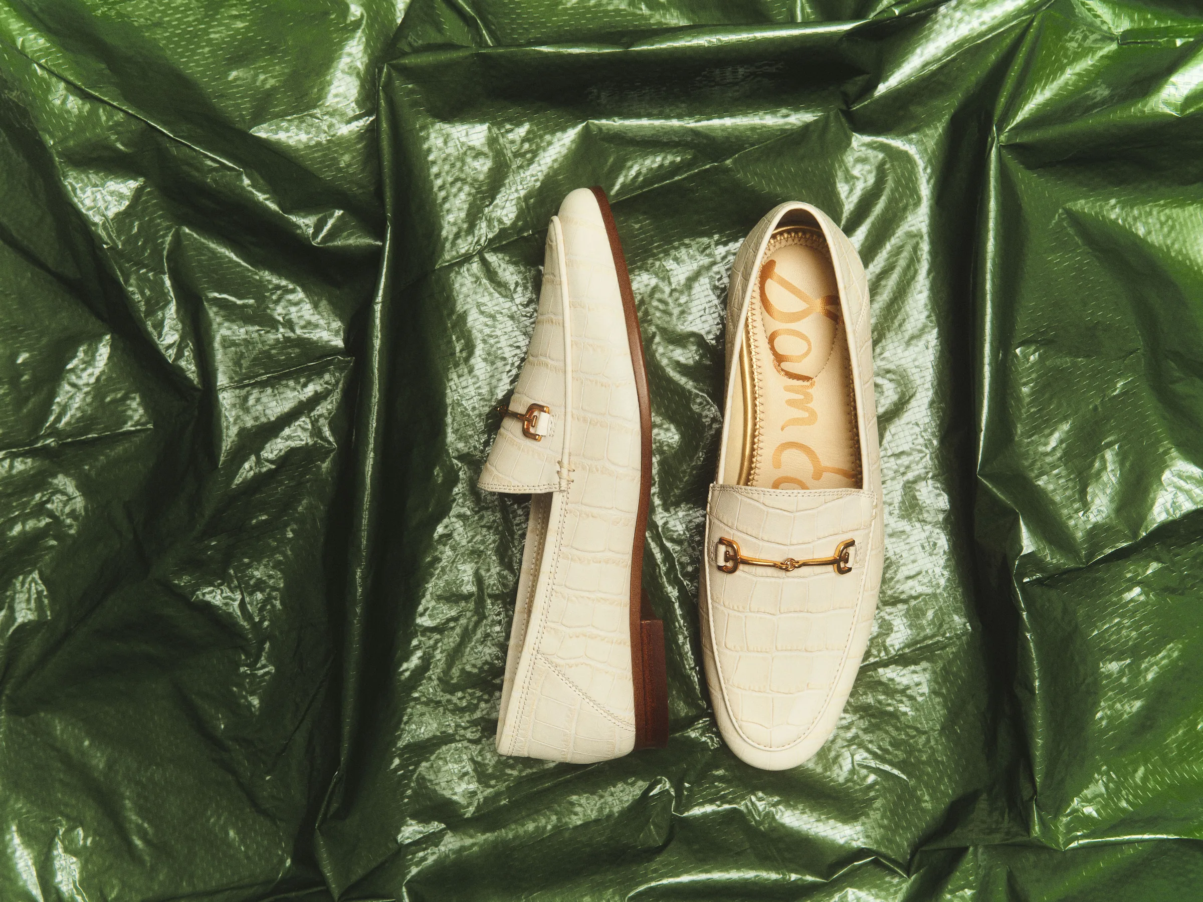 Ivory croc-embossed loafers with gold horsebit hardware on crumpled green metallic plastic, for Sam Edelman.