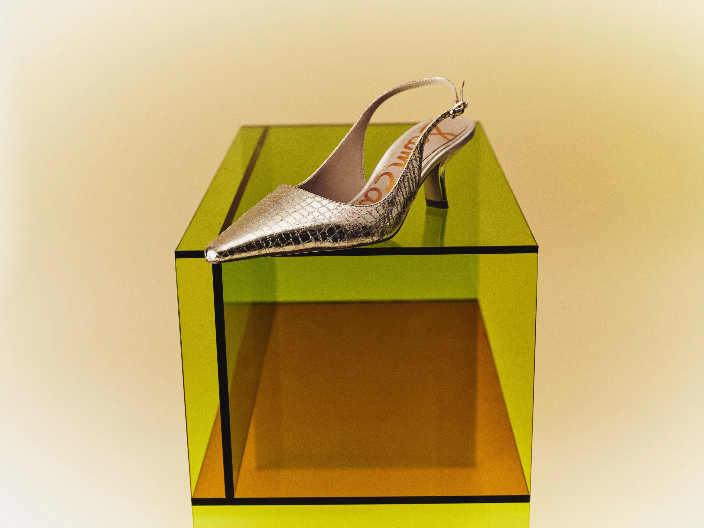 Metallic gold croc-embossed slingback kitten heel on a yellow-green acrylic plinth against a warm backdrop, for Sam Edelman.