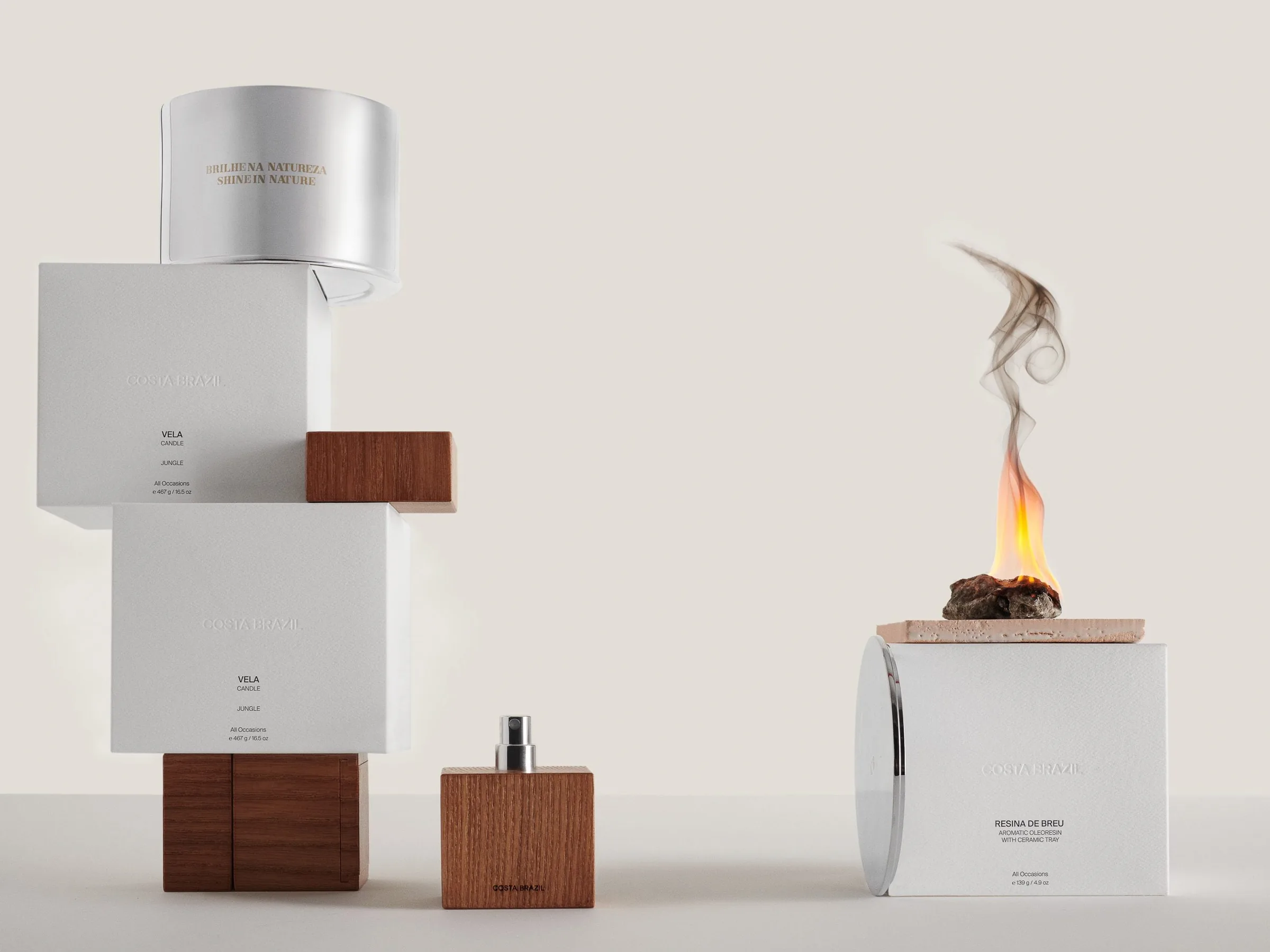 White candle boxes stacked on wooden blocks beside a wood-capped perfume and burning resin on a ceramic tray, for Costa Brazil.