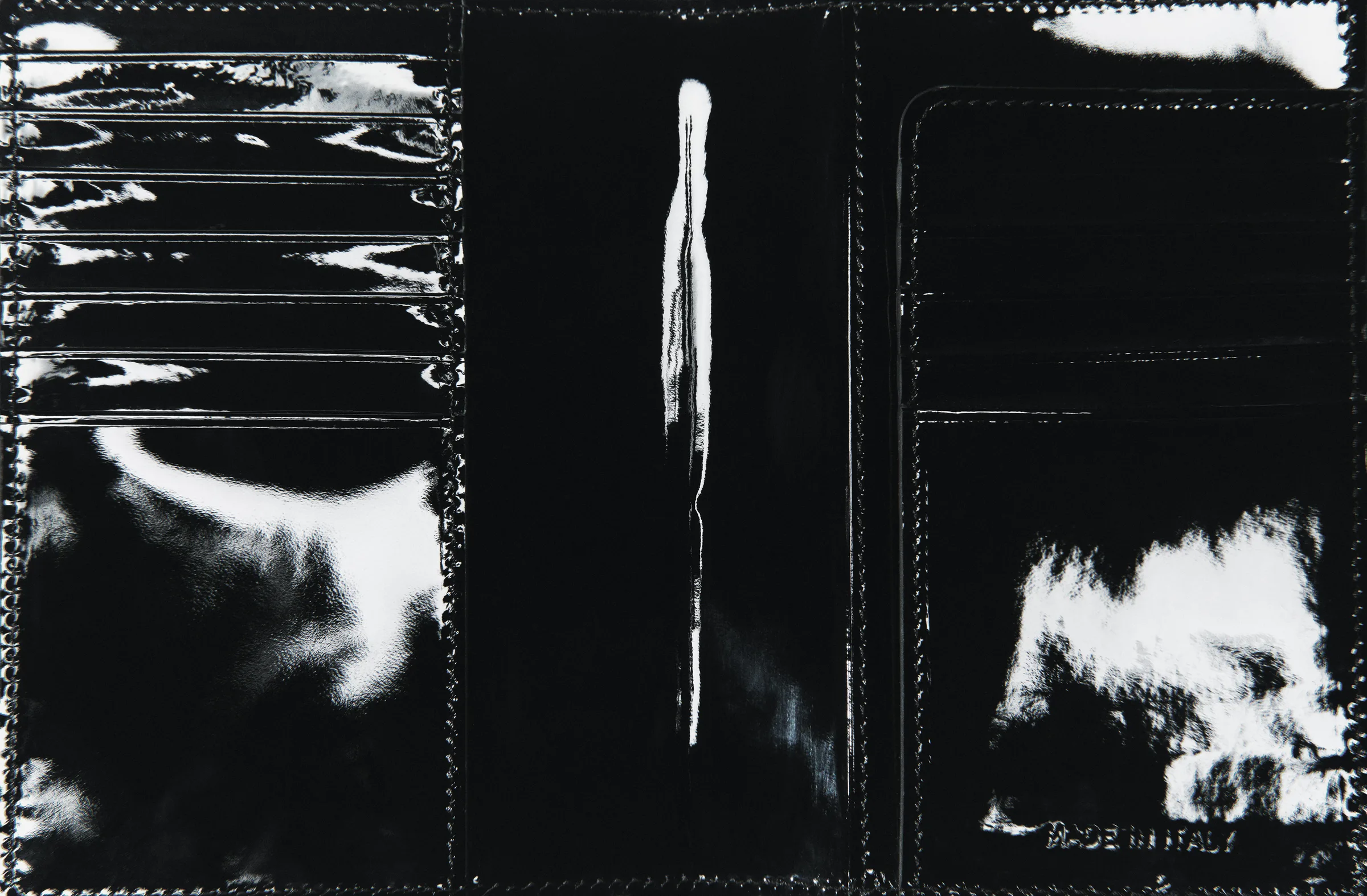 Open black patent leather travel sleeve showing card slots and glossy reflections, stamped Made in Italy, for Strata Creative.