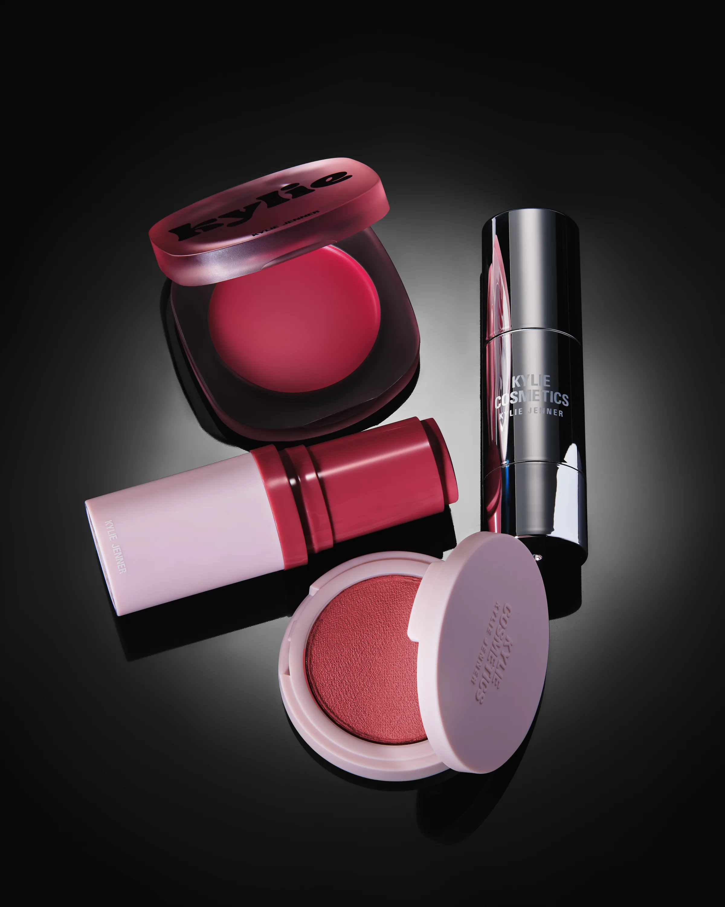 Still life of berry glow balm, hybrid blush, balm stick and powder blush on a black spotlit backdrop, for Kylie Cosmetics.