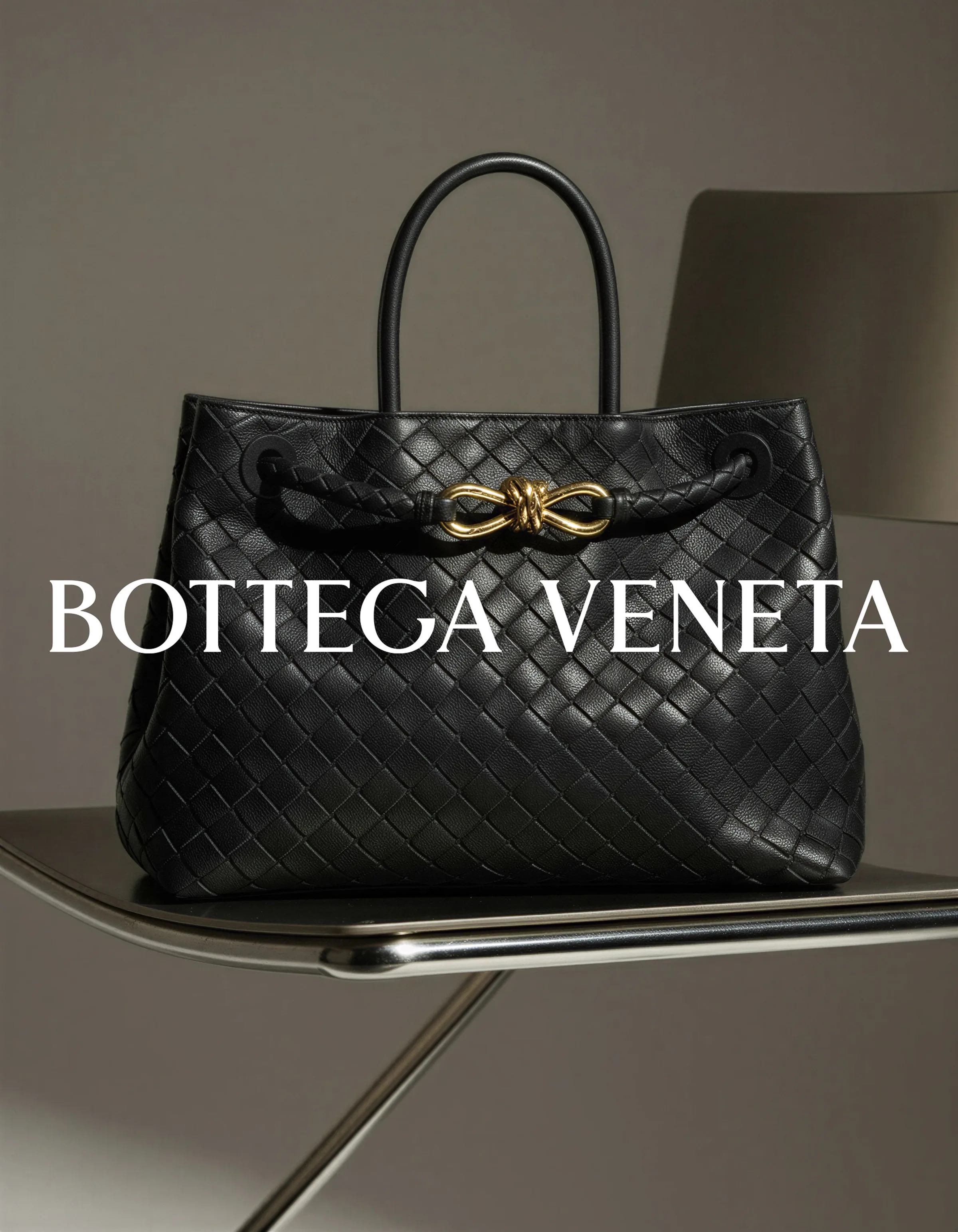 AI image of a black woven leather tote with a gold knot clasp on a chrome chair, with the brand wordmark. Bottega Veneta AI Concept.