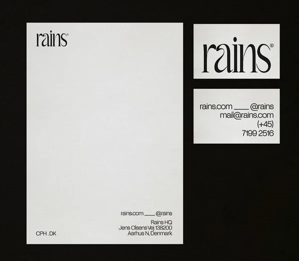 Letterhead and business card front and back with black serif wordmark on off-white paper over a black background, for Rains.