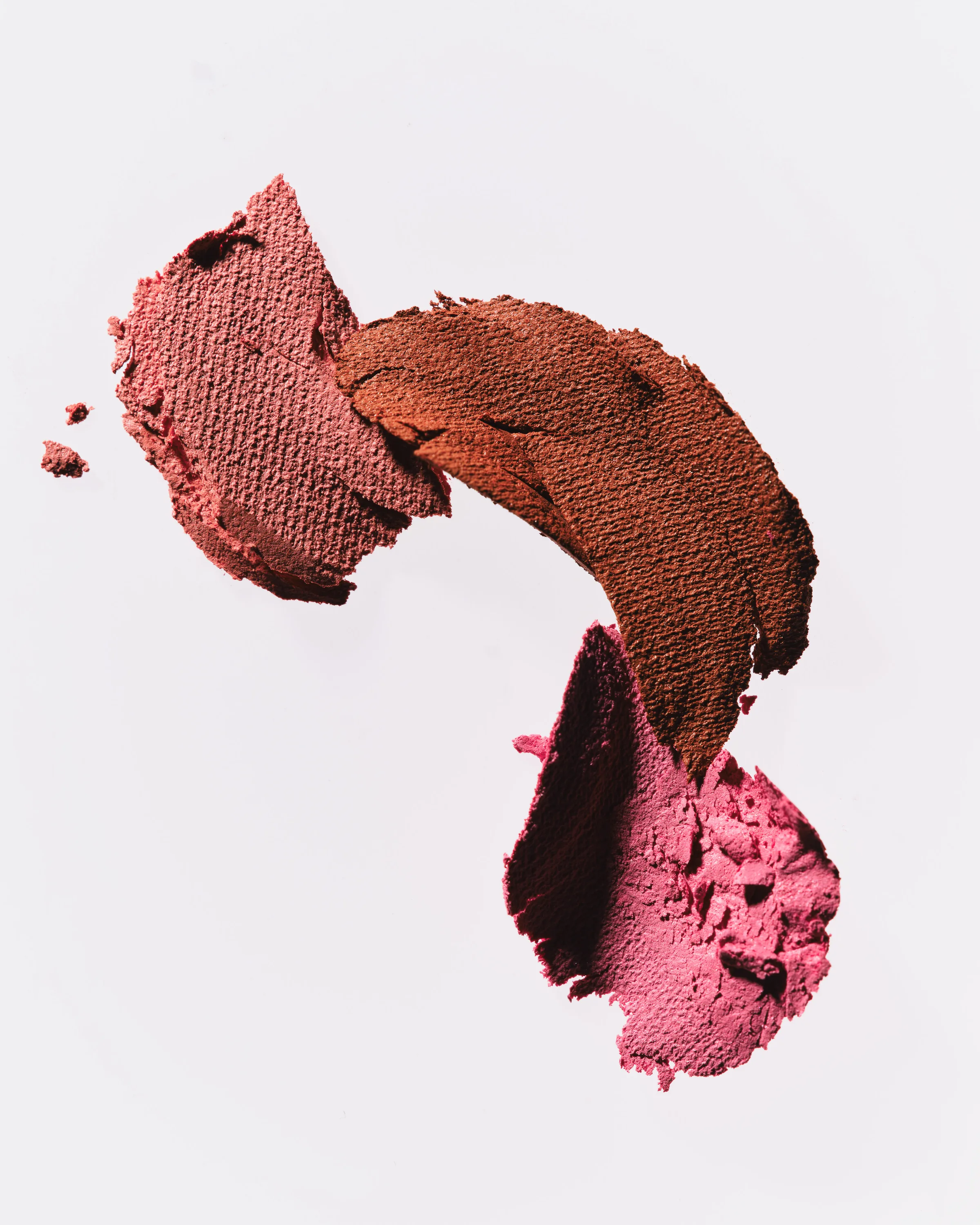 Smeared blush swatches in coral, sienna and pink showing creamy texture on a pale grey background, for Kylie Cosmetics.