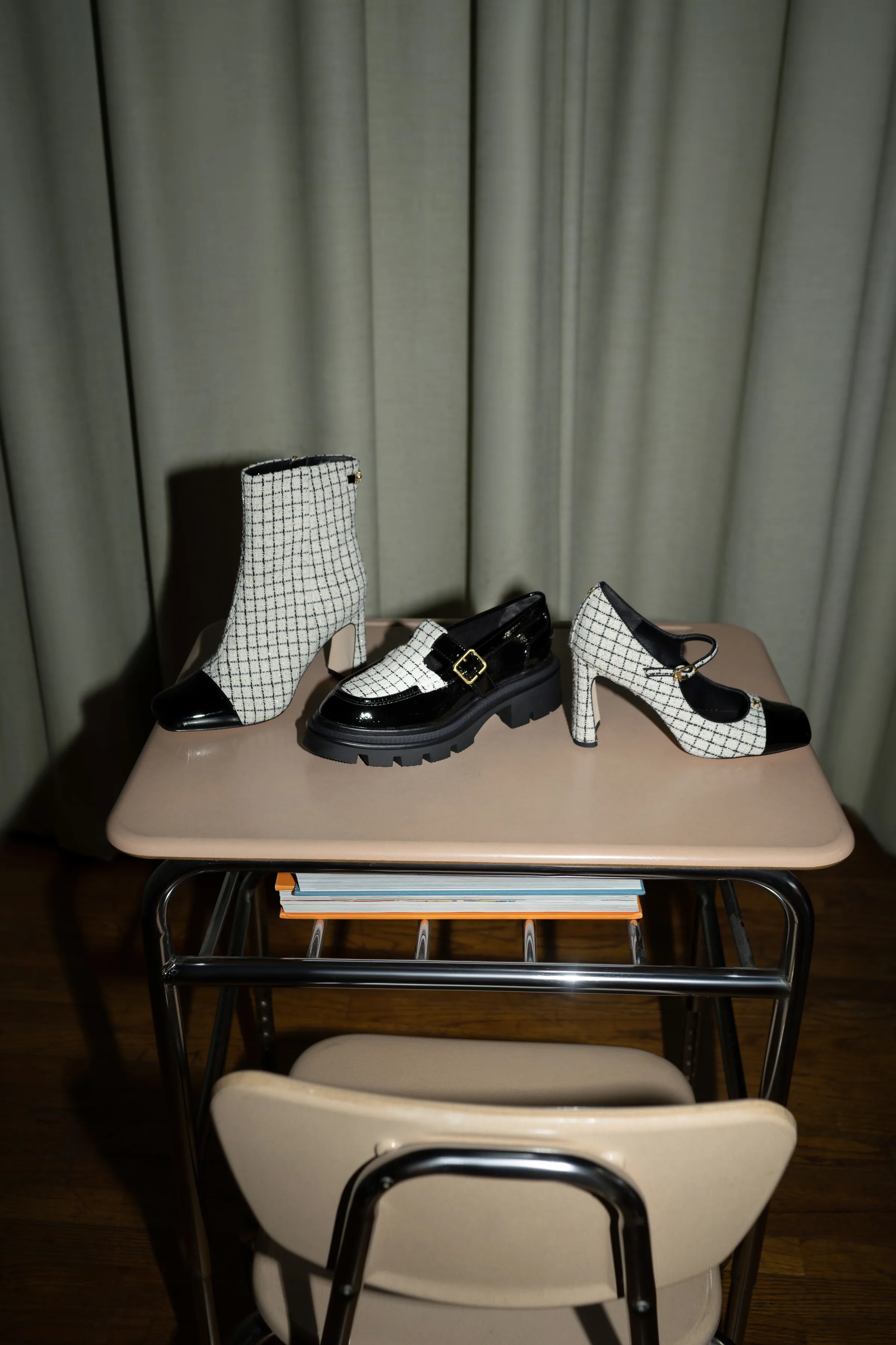 Three black and cream grid tweed shoes, a boot, loafer and Mary Jane, on a beige school desk before a green curtain, for Sam Edelman.
