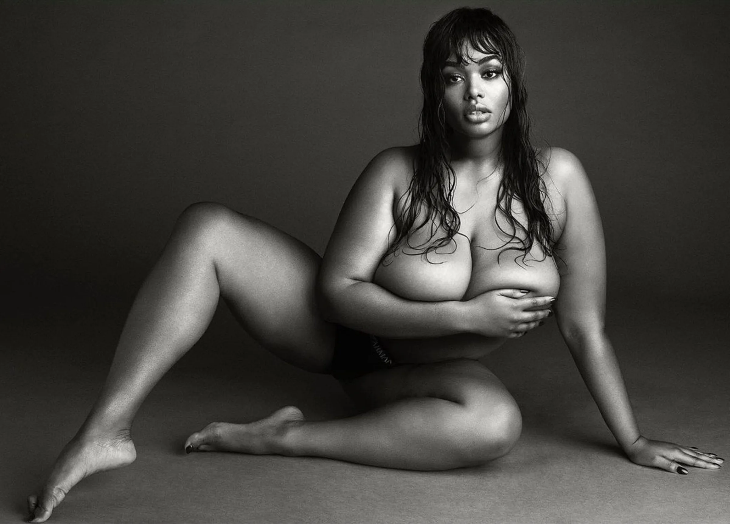 Black and white portrait of a topless model with wet hair seated on the floor, arm across her chest, for V Magazine.