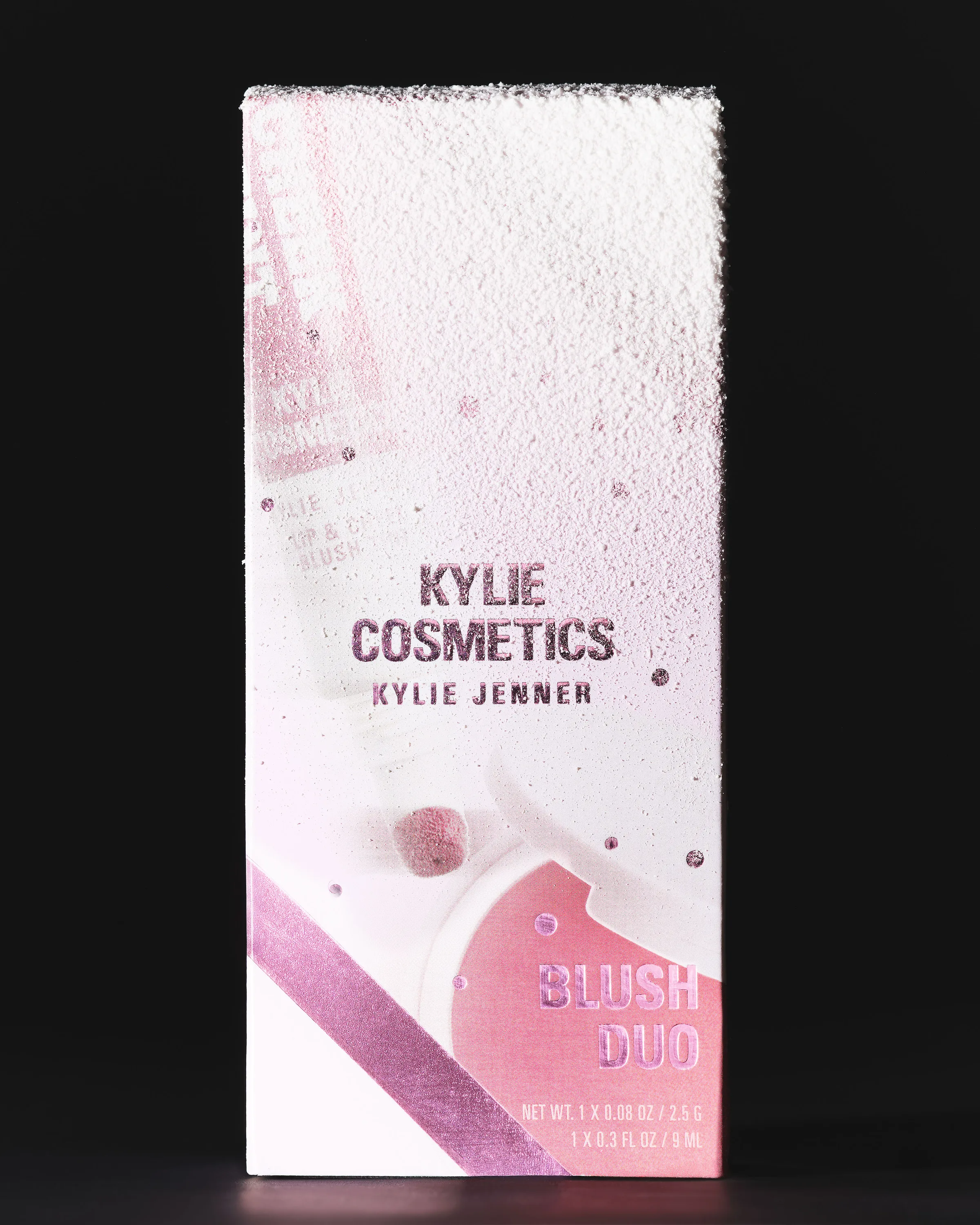 Blush Duo box dusted with white powder, pink metallic lettering, lit against a black background, for Kylie Cosmetics.