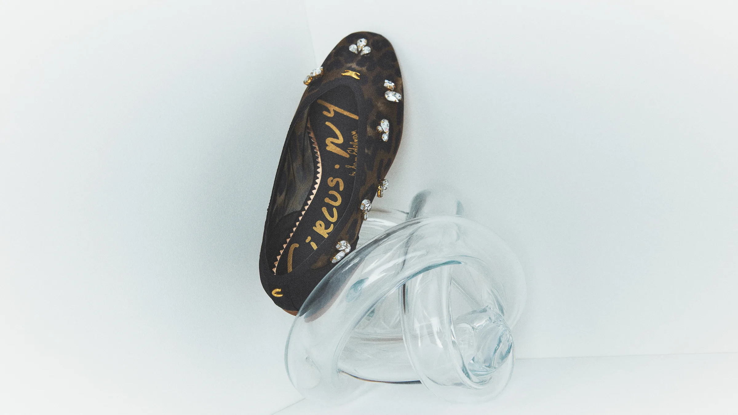 Black leopard-print mesh flat with crystal embellishments resting on a clear glass knot sculpture, for Circus NY.
