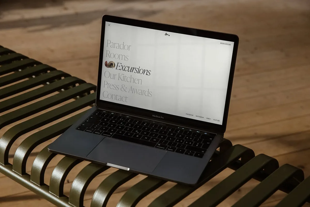 Laptop on a green slatted bench showing a website menu with Parador, Rooms, Excursions and Our Kitchen links, for Cirqa.