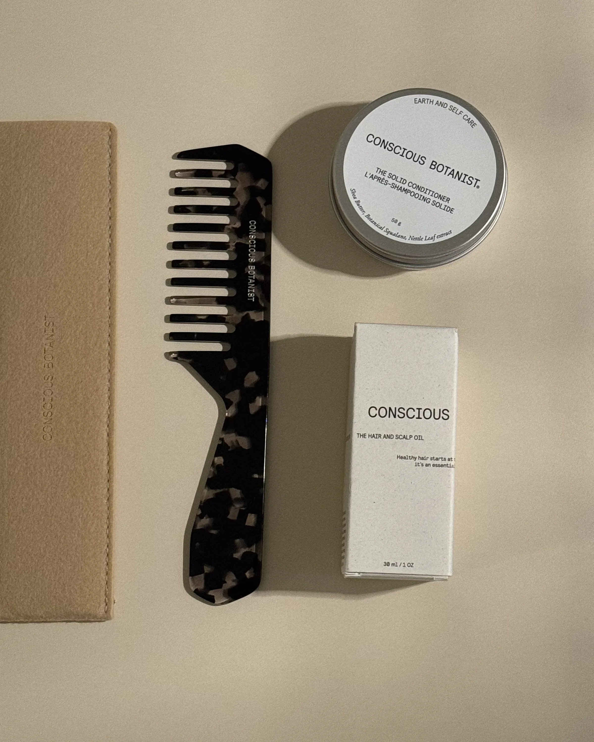Tortoiseshell comb, solid conditioner tin and hair oil box laid flat on beige with a suede pouch, for Conscious Botanist.