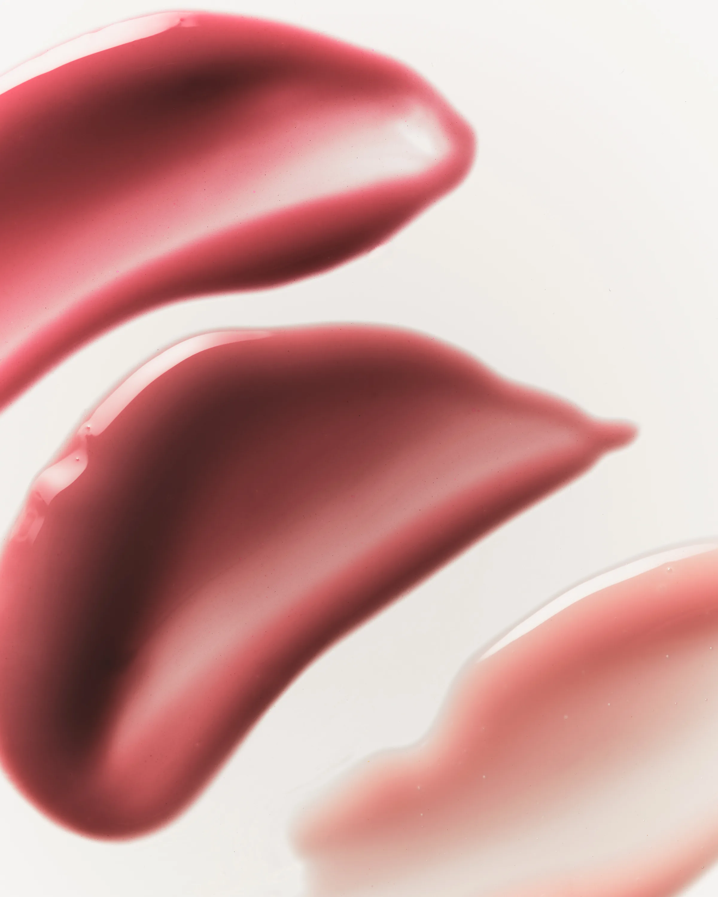 Close-up swatches of three glossy pink and berry plumping lip glosses on a white surface, for Kylie Cosmetics.