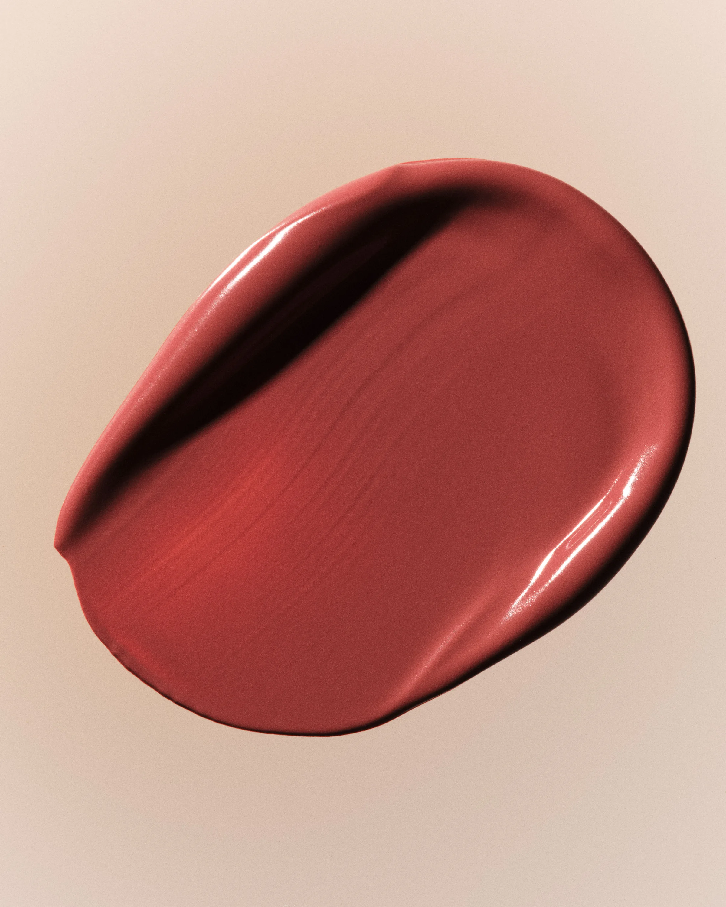 Smeared swatch of rosy red Sweet Talk lipstick with a glossy texture on a soft beige background, for Kylie Cosmetics.