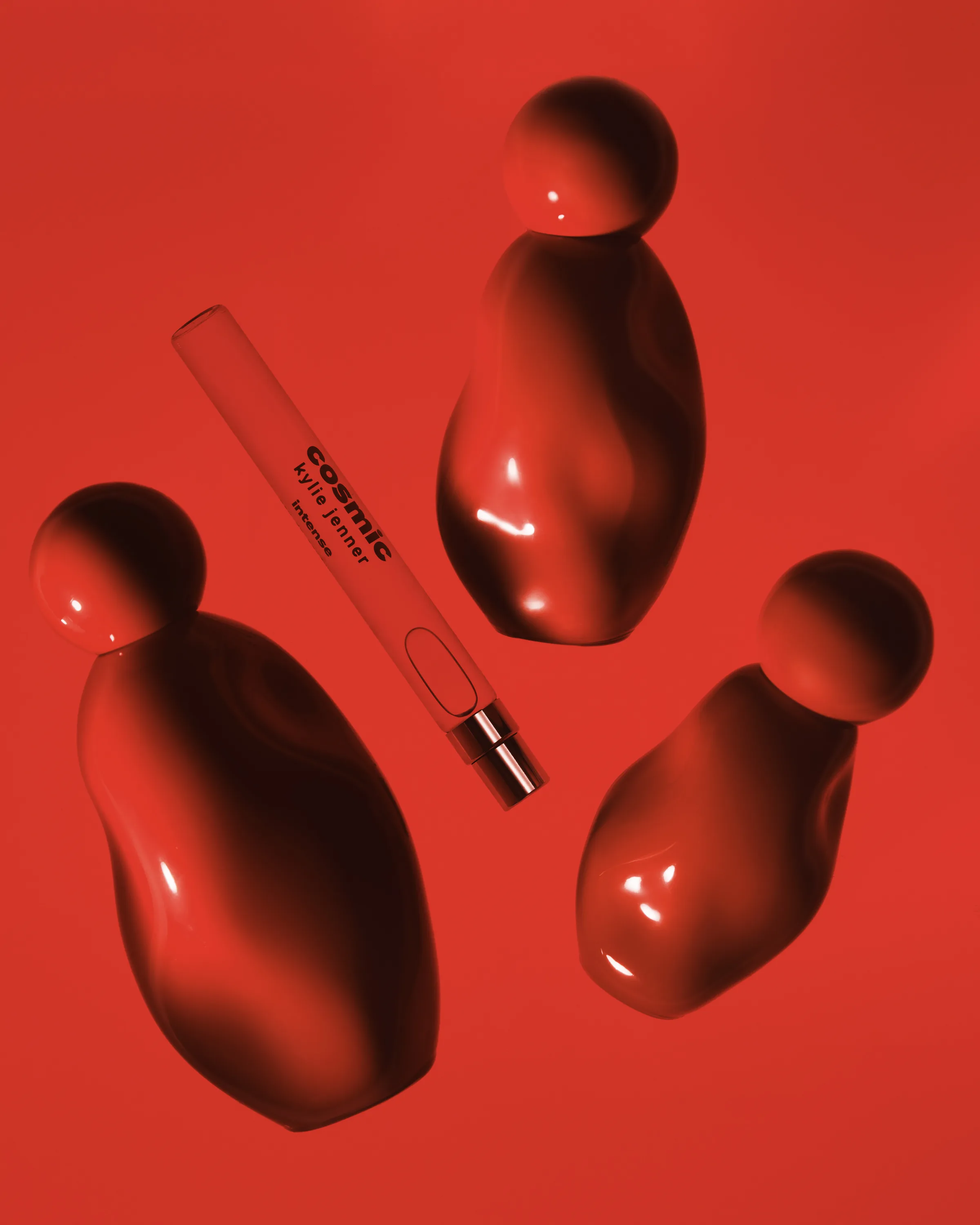 Three red Cosmic Intense perfume bottles and a travel spray laid on a glossy red background, for Kylie Cosmetics.