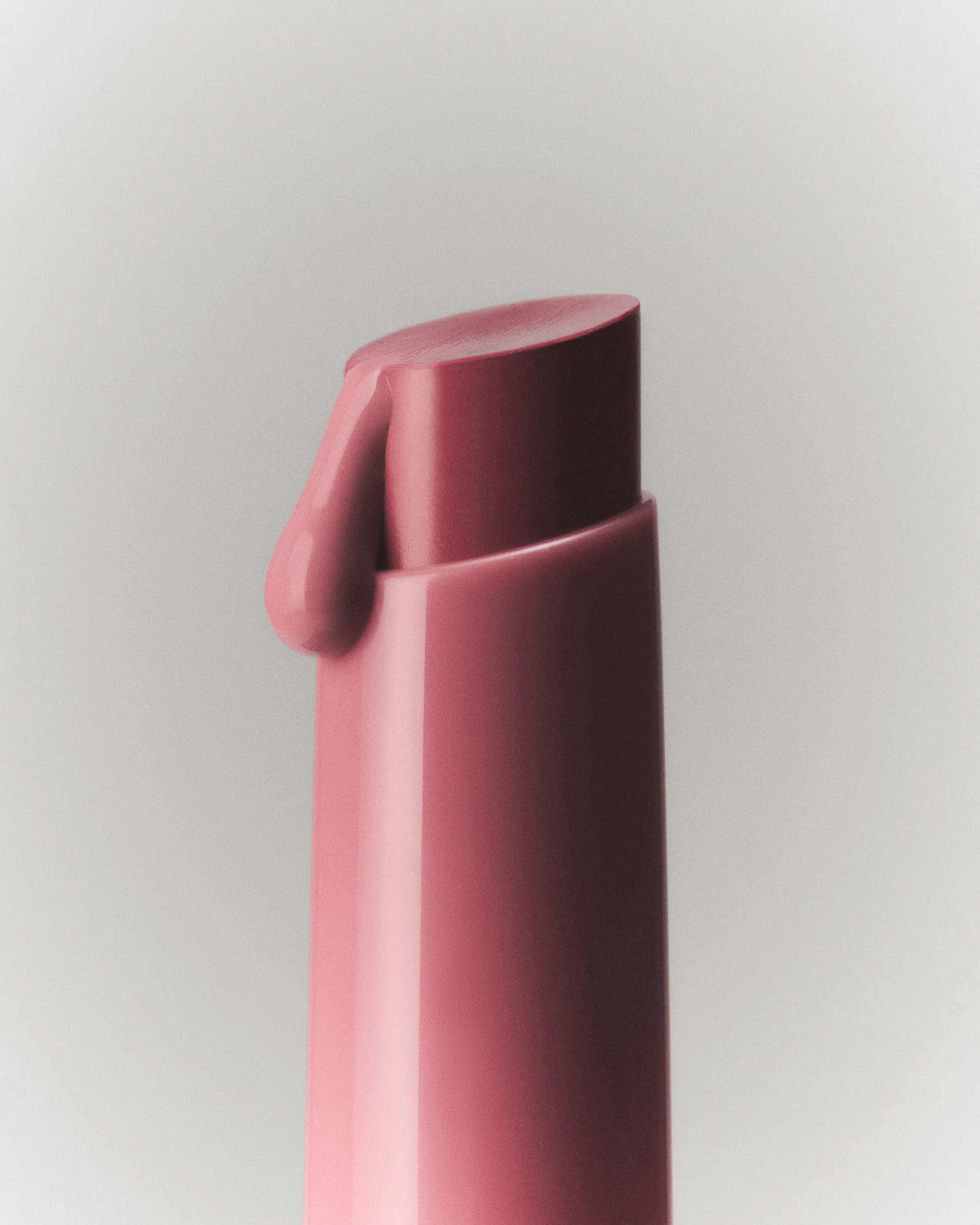 Close-up still life of a mauve lip crayon with a glossy drop running down its tip on a grey backdrop, for Kylie Cosmetics.