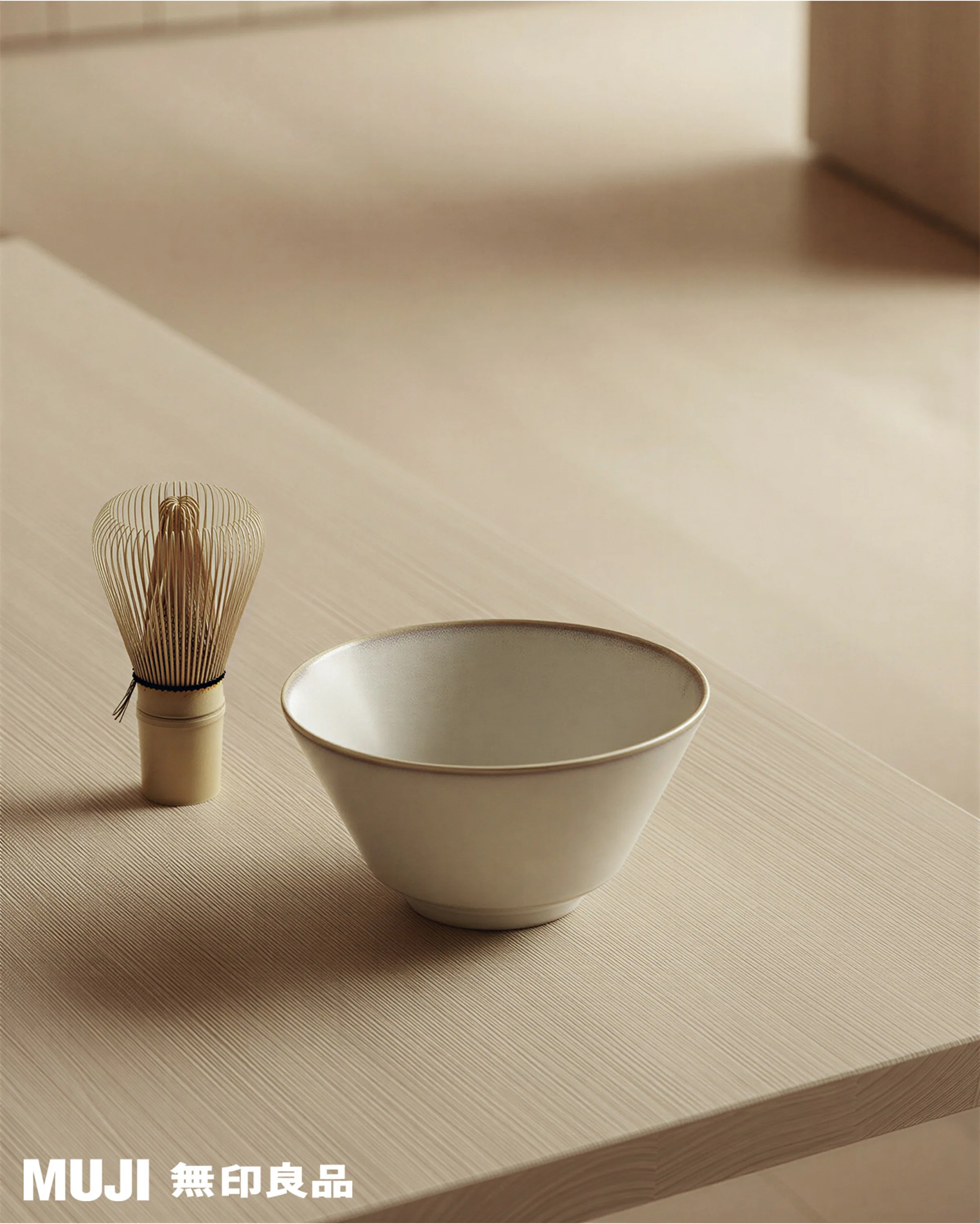 AI image of a cream ceramic matcha bowl beside a bamboo whisk on a pale wooden table. MUJI AI Concept.