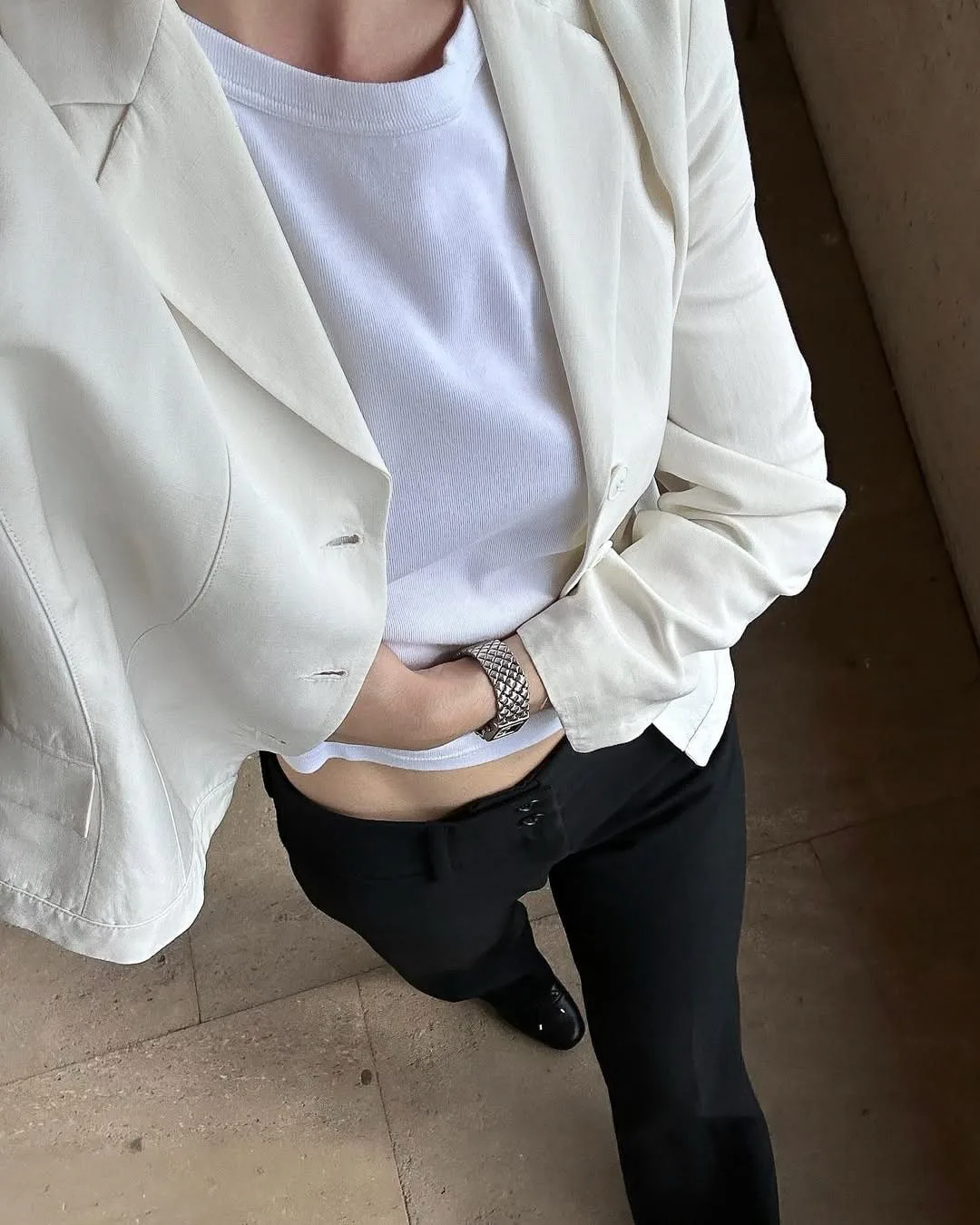 Phone-style top-down shot of a woman in a cream blazer, white tee and black trousers wearing a silver woven cuff bracelet.
