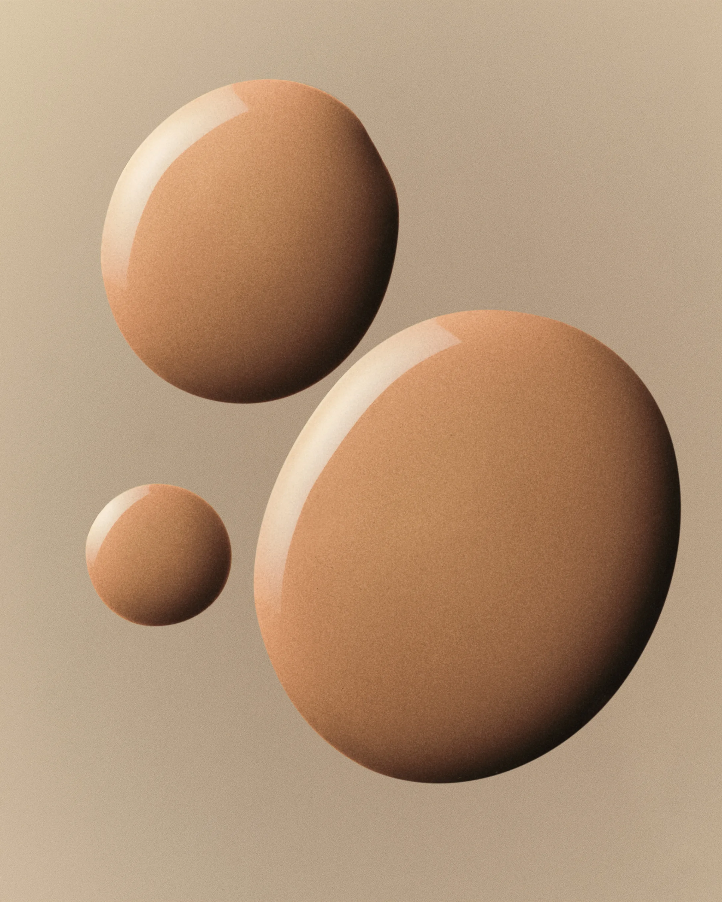 Three glossy drops of tan foundation swatched on a beige background, for Kylie Cosmetics.