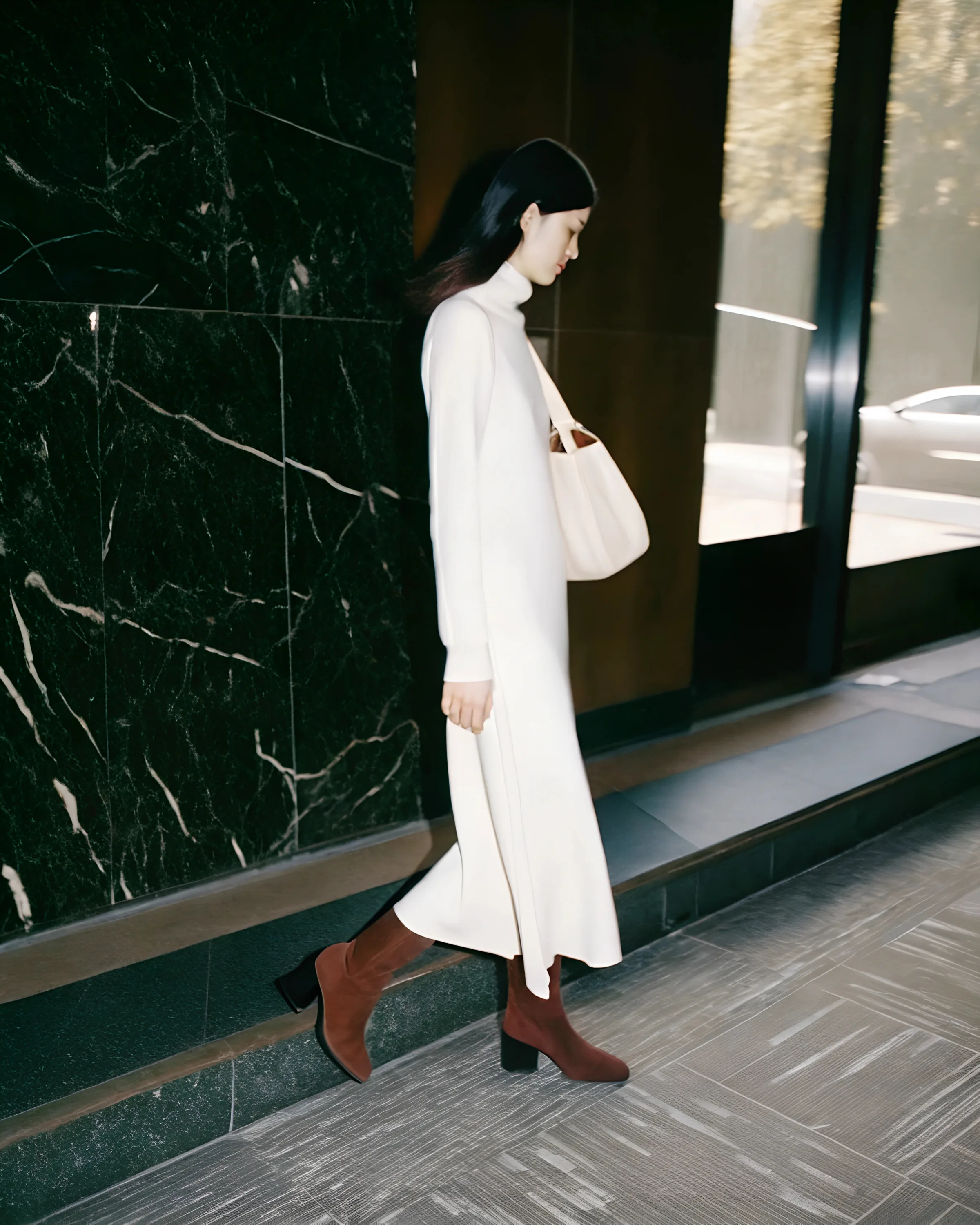 AI image of a model in a cream knit dress and rust suede boots walking past black marble with a white bag. Proenza Schouler AI Concept.