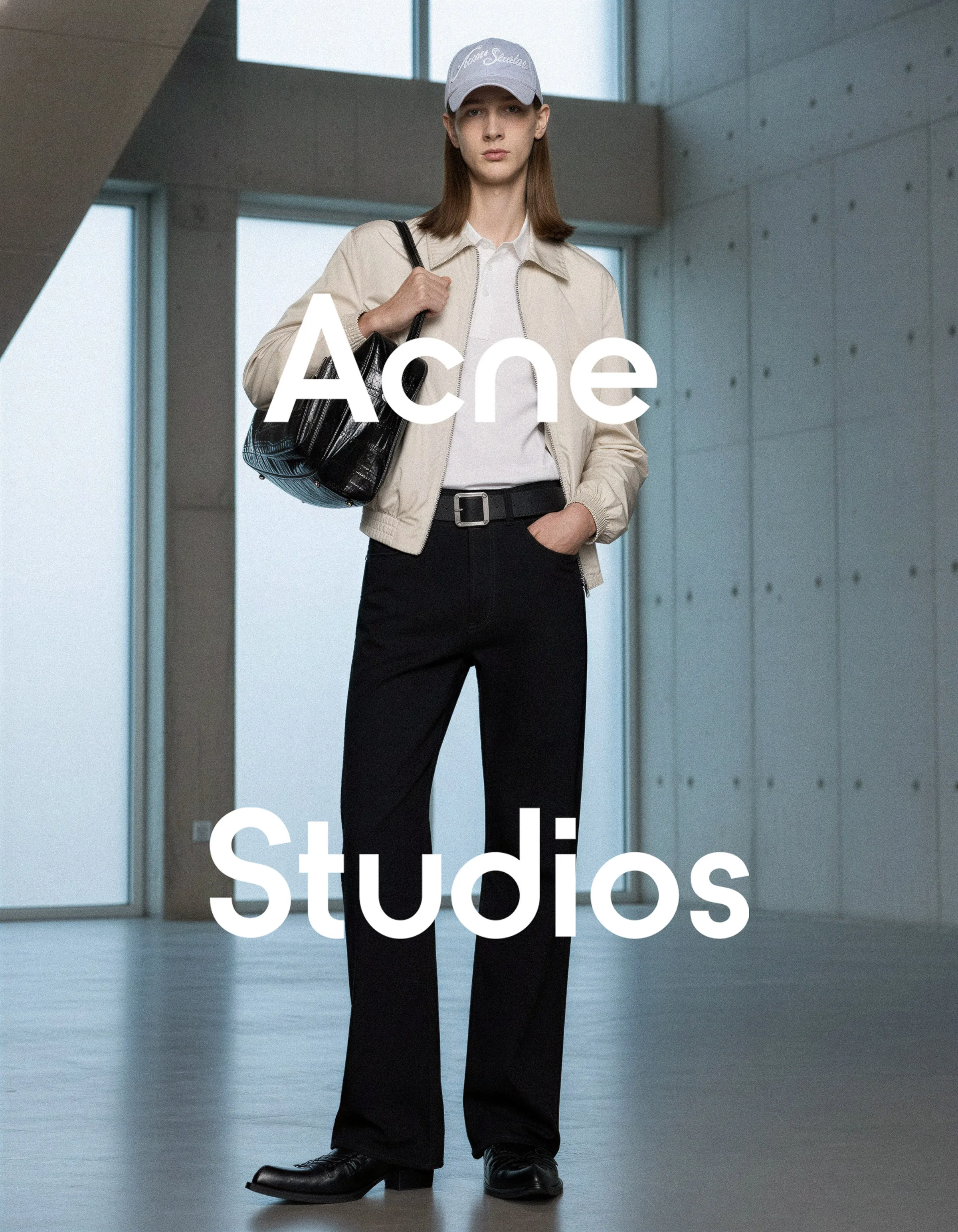 AI image of a model in a cream jacket, black jeans and cap holding a black leather bag in a concrete hall. Acne Studios AI Concept.