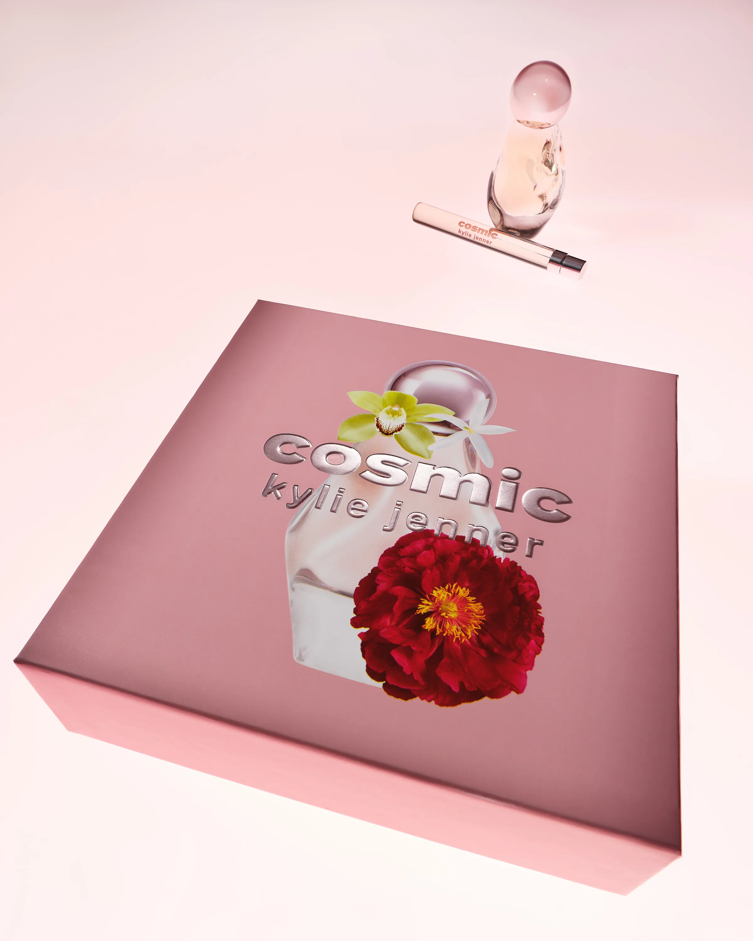 Pink Cosmic gift box with peony and orchid art beside the perfume bottle and pen spray on pink, for Kylie Cosmetics.