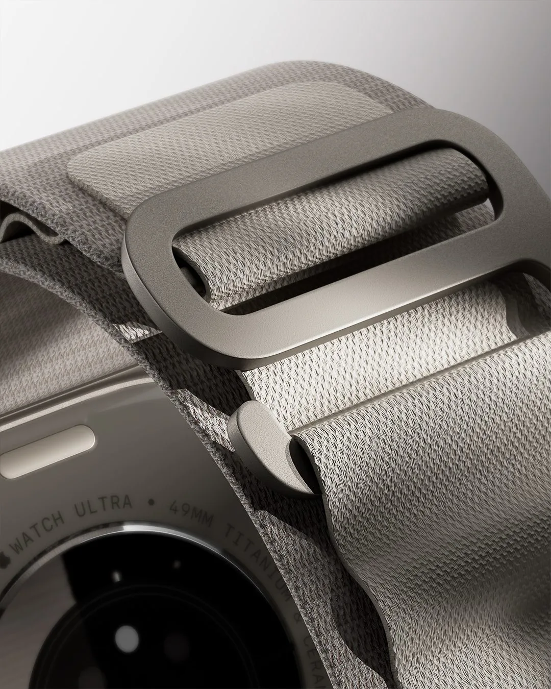 CGI render of an Apple Watch Ultra with a grey woven loop band and titanium buckle in close-up, for Apple.