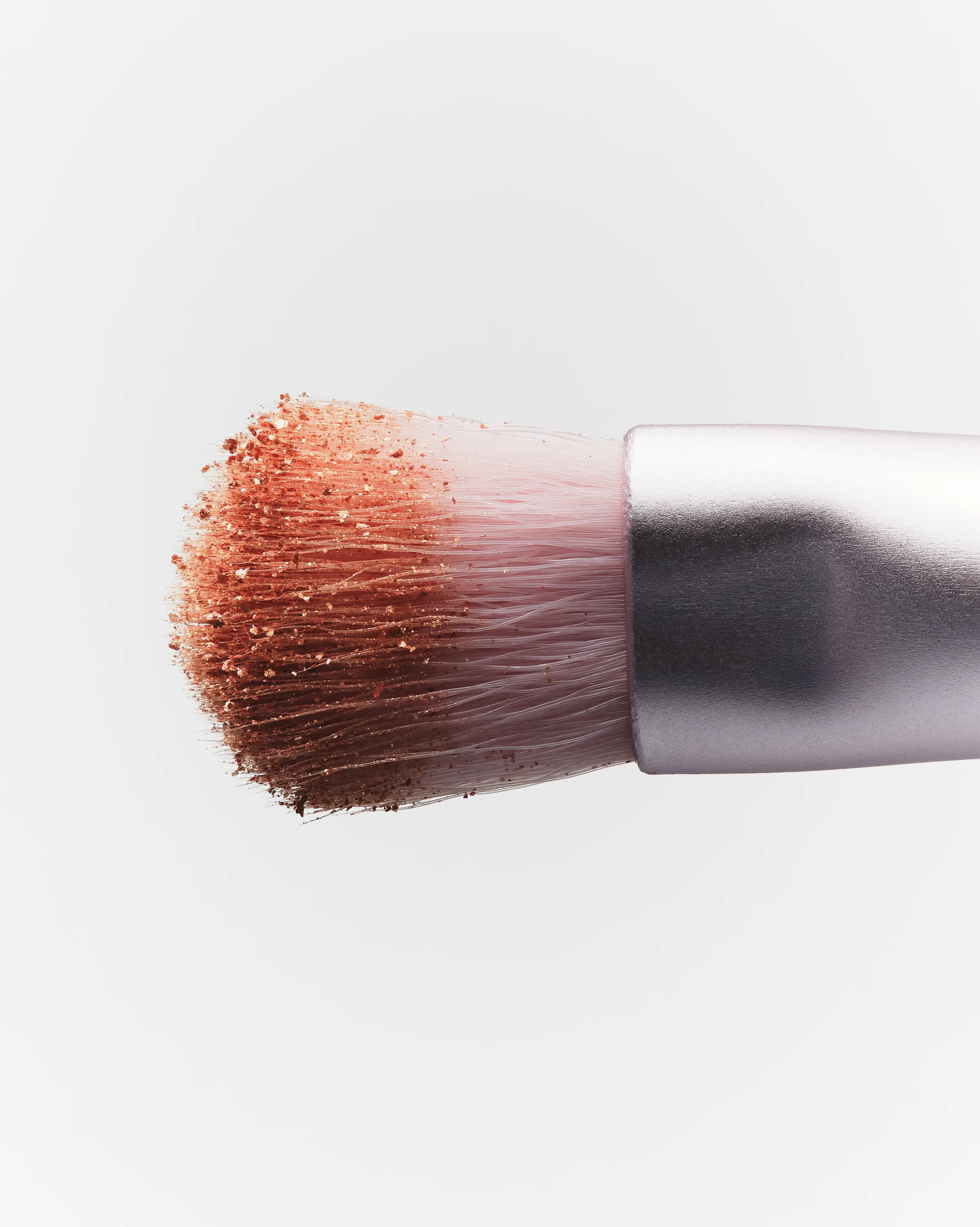 Close-up of a makeup brush loaded with shimmering copper eyeshadow pigment on a pale grey background, for Kylie Cosmetics.